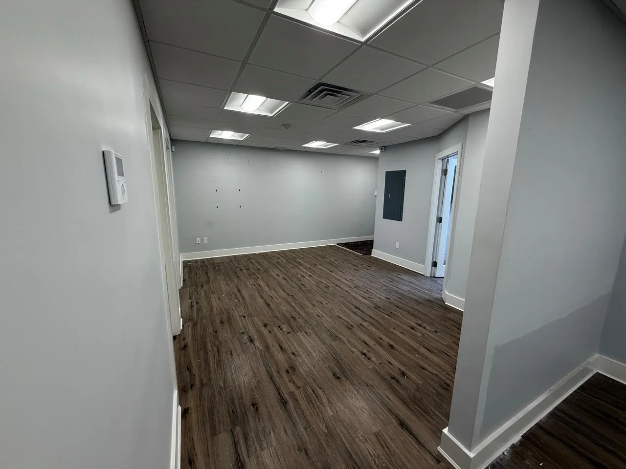 Empty room with dark wood-type flooring, a paneled ceiling, and electric panel Empty room with dark wood-type flooring, a paneled ceiling, and electric panel