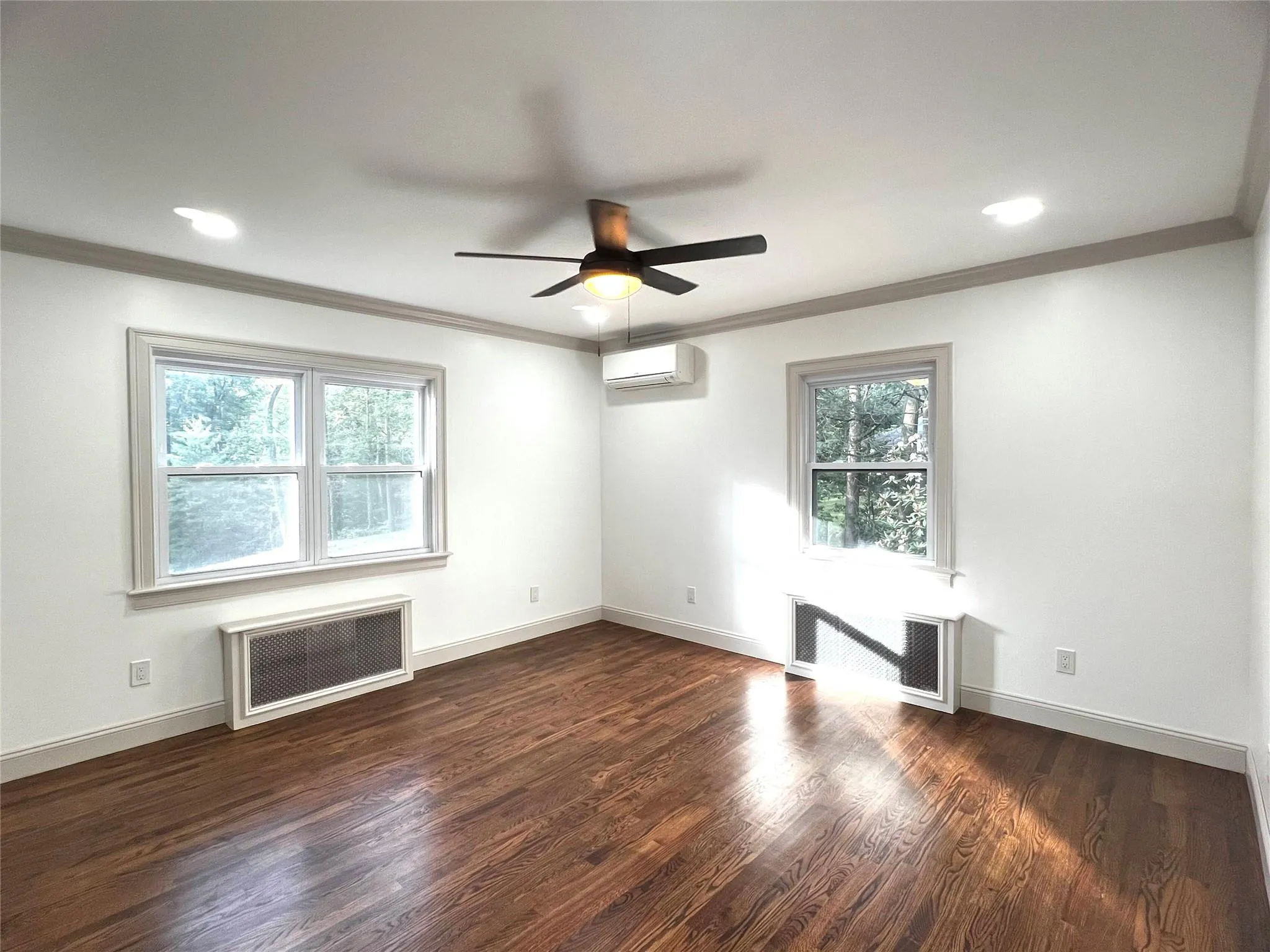 Unfurnished living room with a ceiling fan, crown molding, radiator heating unit, dark wood-style flooring, and recessed lighting Unfurnished living room with a ceiling fan, crown molding, radiator heating unit, dark wood-style flooring, and recessed lighting