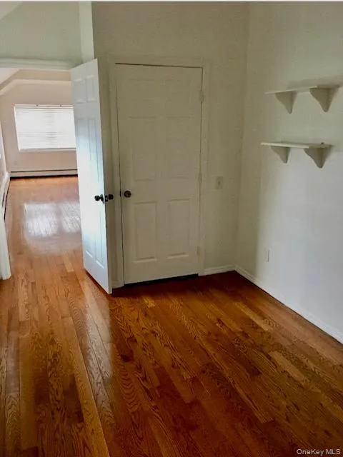 Unfurnished bedroom featuring wood finished floors and baseboard heating Unfurnished bedroom featuring wood finished floors and baseboard heating