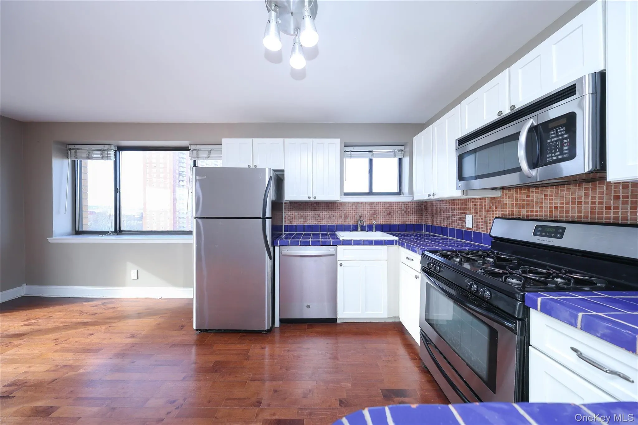 Kitchen with tile countertops, appliances with stainless steel finishes, white cabinetry, dark wood-style floors, and healthy amount of natural light Kitchen with tile countertops, appliances with stainless steel finishes, white cabinetry, dark wood-style floors, and healthy amount of natural light