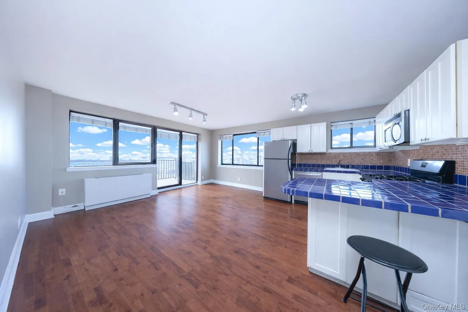 Kitchen featuring tile counters, white cabinets, stainless steel appliances, track lighting, and dark wood-style flooring Kitchen featuring tile counters, white cabinets, stainless steel appliances, track lighting, and dark wood-style flooring