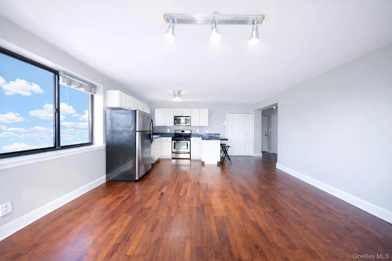 Kitchen with appliances with stainless steel finishes, white cabinetry, dark countertops, dark wood-type flooring, and open floor plan Kitchen with appliances with stainless steel finishes, white cabinetry, dark countertops, dark wood-type flooring, and open floor plan