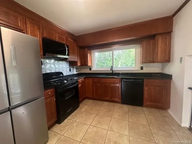 Kitchen with black appliances, dark countertops, backsplash, and brown cabinets Kitchen with black appliances, dark countertops, backsplash, and brown cabinets