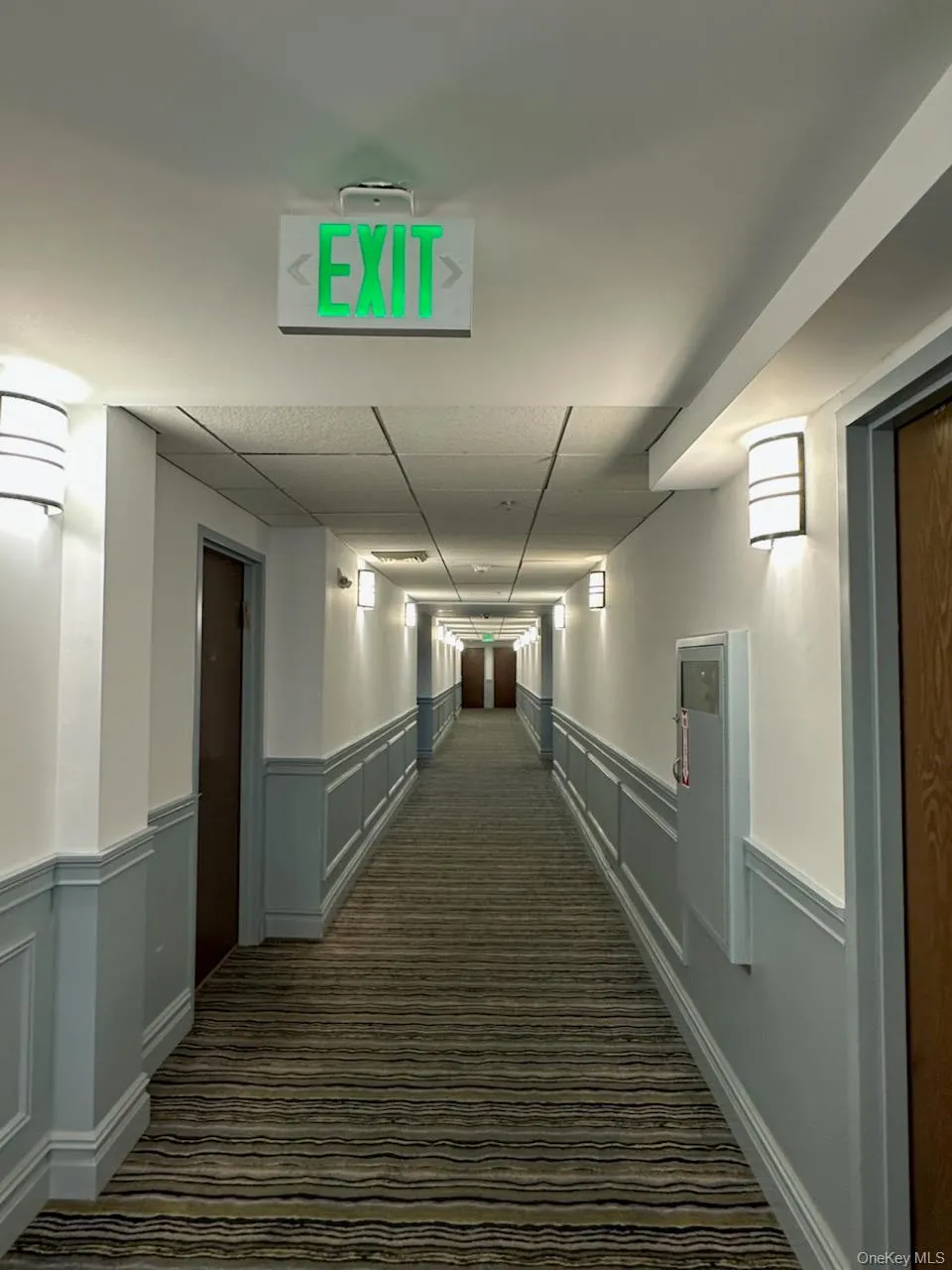 Hall with dark colored carpet, a wainscoted wall, and a paneled ceiling Hall with dark colored carpet, a wainscoted wall, and a paneled ceiling