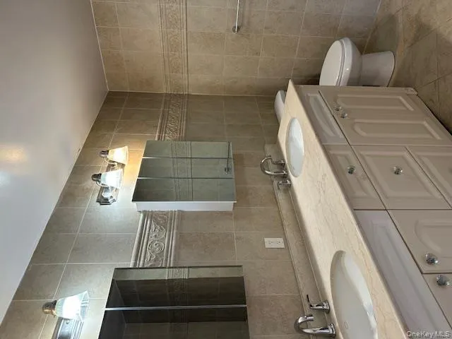 Bathroom featuring tile walls, double vanity, light tile patterned flooring, and decorative backsplash Bathroom featuring tile walls, double vanity, light tile patterned flooring, and decorative backsplash