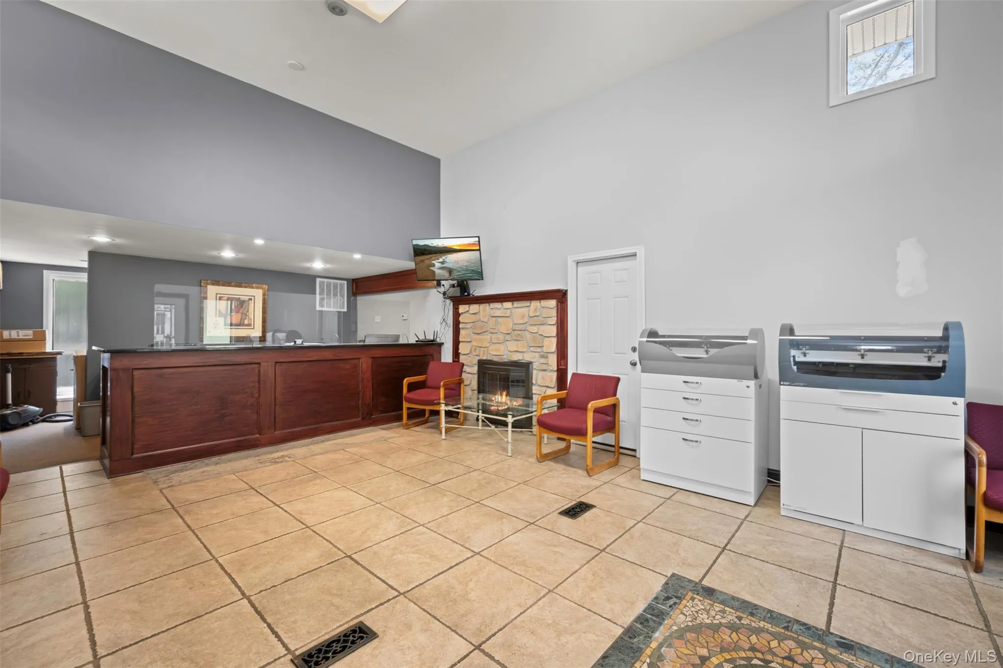 Kitchen with high vaulted ceiling, a fireplace, light tile patterned floors, dark countertops, and a peninsula Kitchen with high vaulted ceiling, a fireplace, light tile patterned floors, dark countertops, and a peninsula