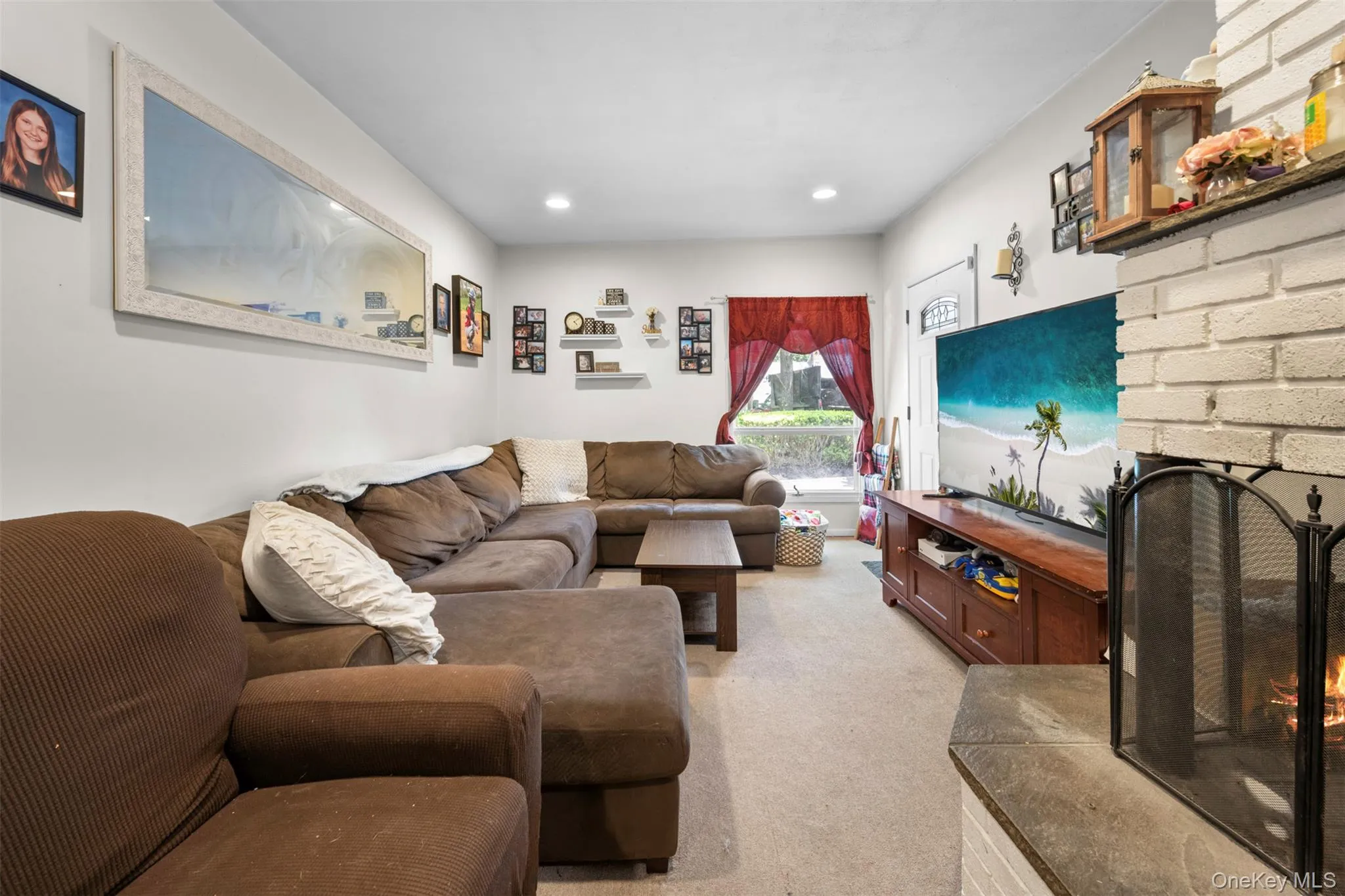 Living area featuring a brick fireplace, light colored carpet, and recessed lighting Living area featuring a brick fireplace, light colored carpet, and recessed lighting