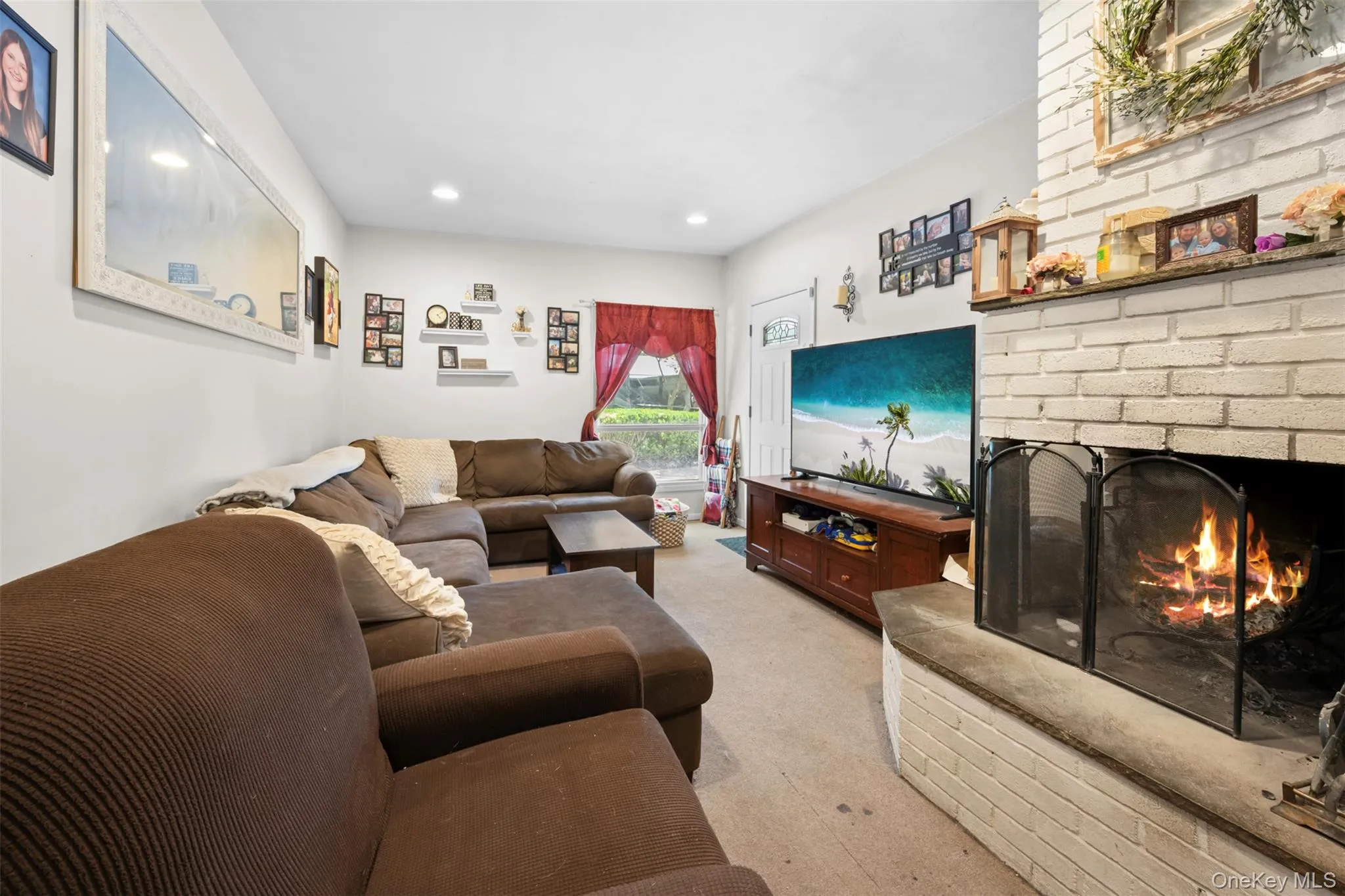 Living room with a brick fireplace, light colored carpet, and recessed lighting Living room with a brick fireplace, light colored carpet, and recessed lighting