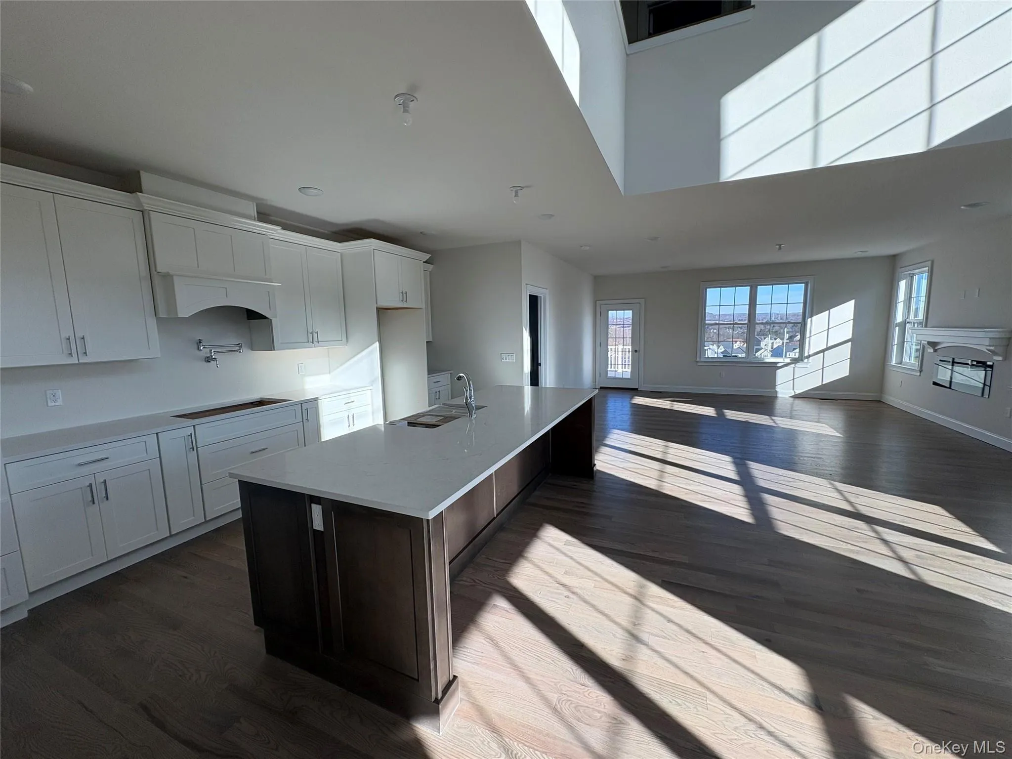 Kitchen featuring white cabinetry, an island with sink, dark wood-style flooring, light stone countertops, and a breakfast bar Kitchen featuring white cabinetry, an island with sink, dark wood-style flooring, light stone countertops, and a breakfast bar