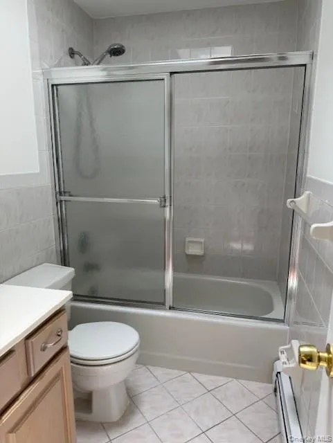 Full bath with tile walls, vanity, tile patterned flooring, combined bath / shower with glass door, and a baseboard heating unit Full bath with tile walls, vanity, tile patterned flooring, combined bath / shower with glass door, and a baseboard heating unit