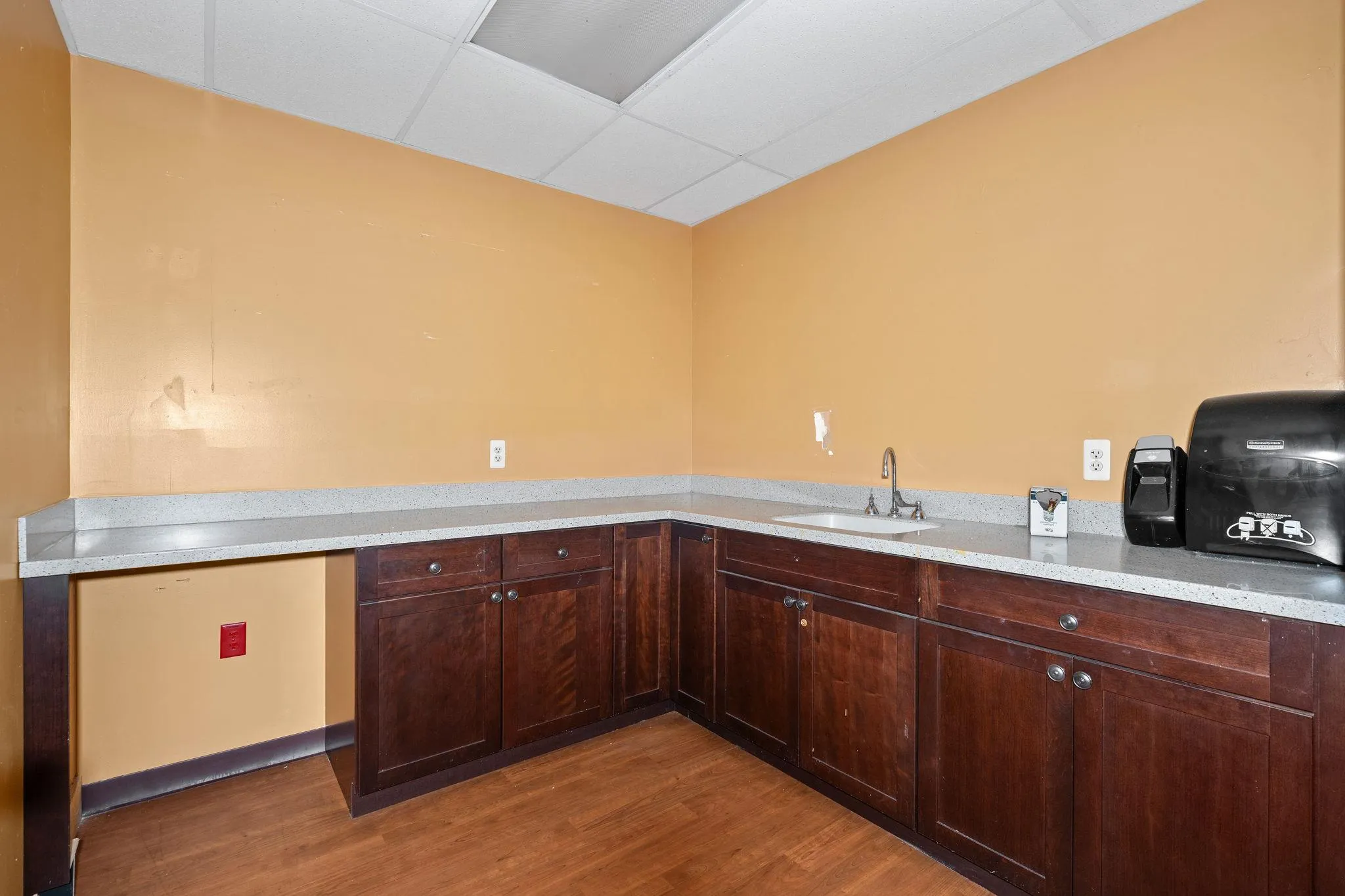 Kitchen featuring a paneled ceiling, light wood-type flooring, dark brown cabinets, light stone counters, and a desk Kitchen featuring a paneled ceiling, light wood-type flooring, dark brown cabinets, light stone counters, and a desk