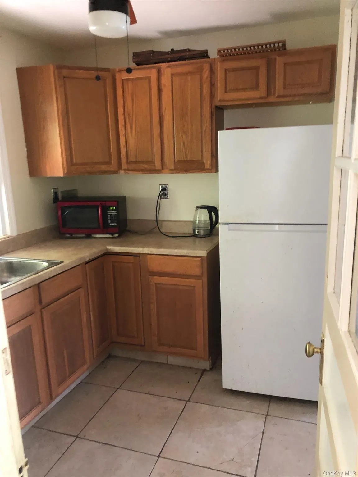 Kitchen featuring freestanding refrigerator, brown cabinets, and light countertops Kitchen featuring freestanding refrigerator, brown cabinets, and light countertops