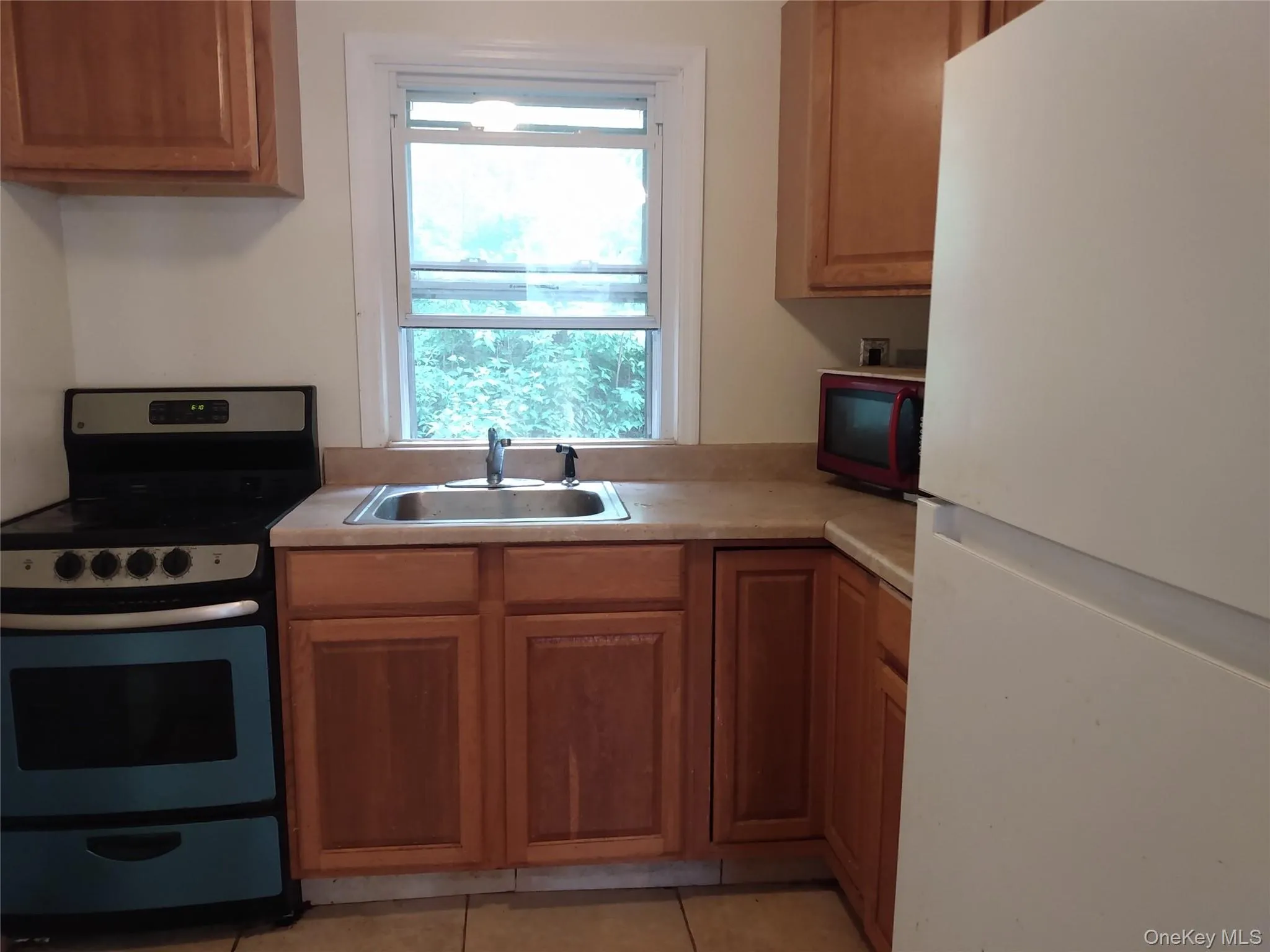 Kitchen with freestanding refrigerator, electric stove, light countertops, and light tile patterned floors Kitchen with freestanding refrigerator, electric stove, light countertops, and light tile patterned floors