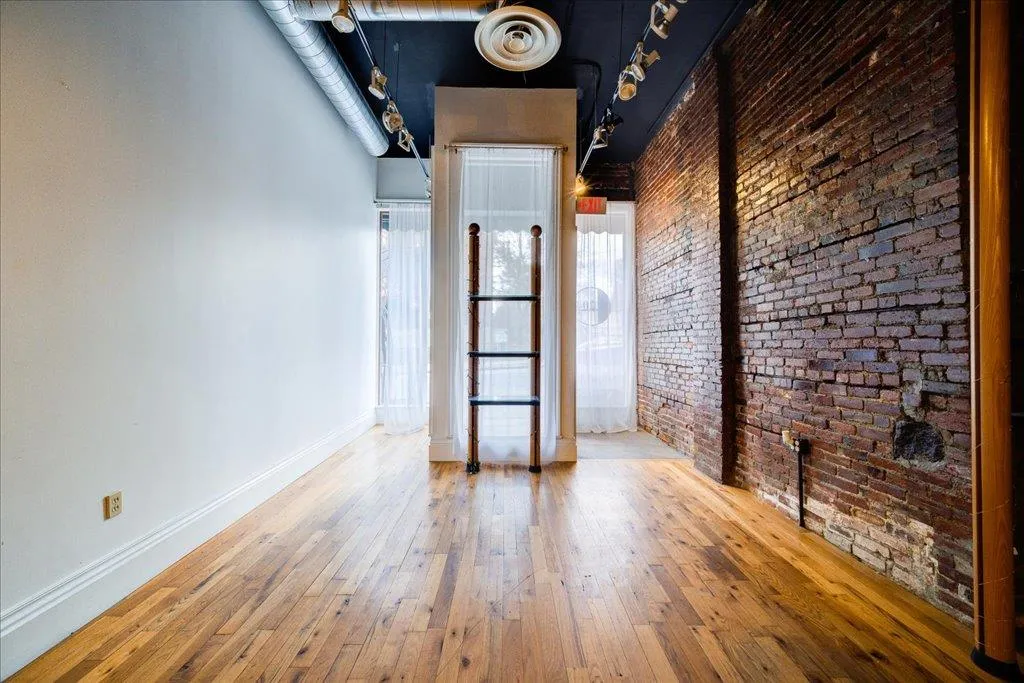 Empty room featuring brick wall and hardwood / wood-style floors Empty room featuring brick wall and hardwood / wood-style floors
