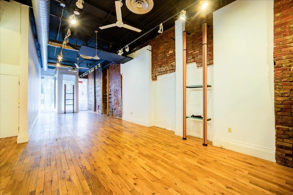 Empty room featuring ceiling fan, brick wall, and light hardwood / wood-style floors Empty room featuring ceiling fan, brick wall, and light hardwood / wood-style floors
