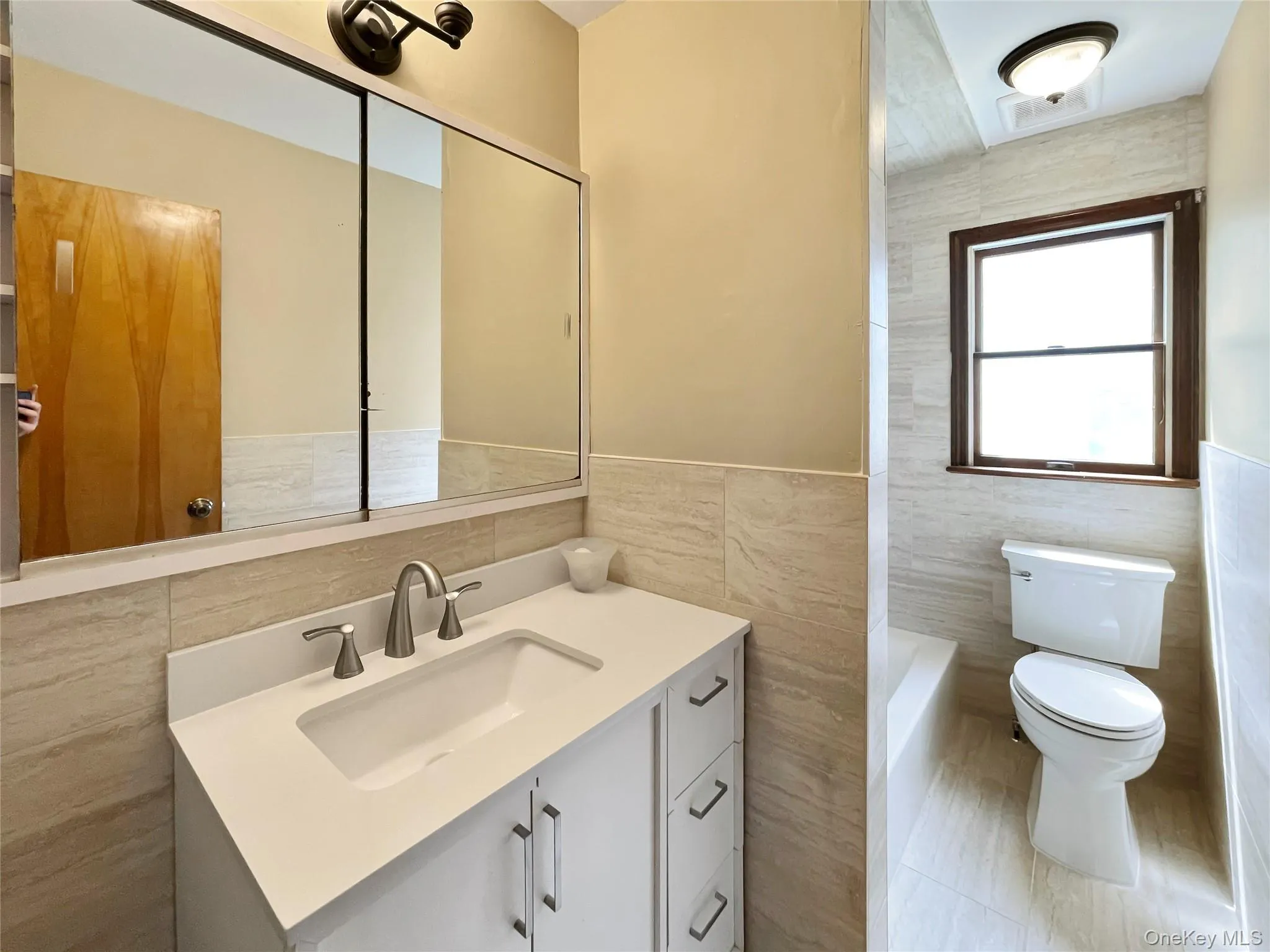Full bath with tile walls, vanity, a tub to relax in, a wainscoted wall, and tile patterned flooring Full bath with tile walls, vanity, a tub to relax in, a wainscoted wall, and tile patterned flooring