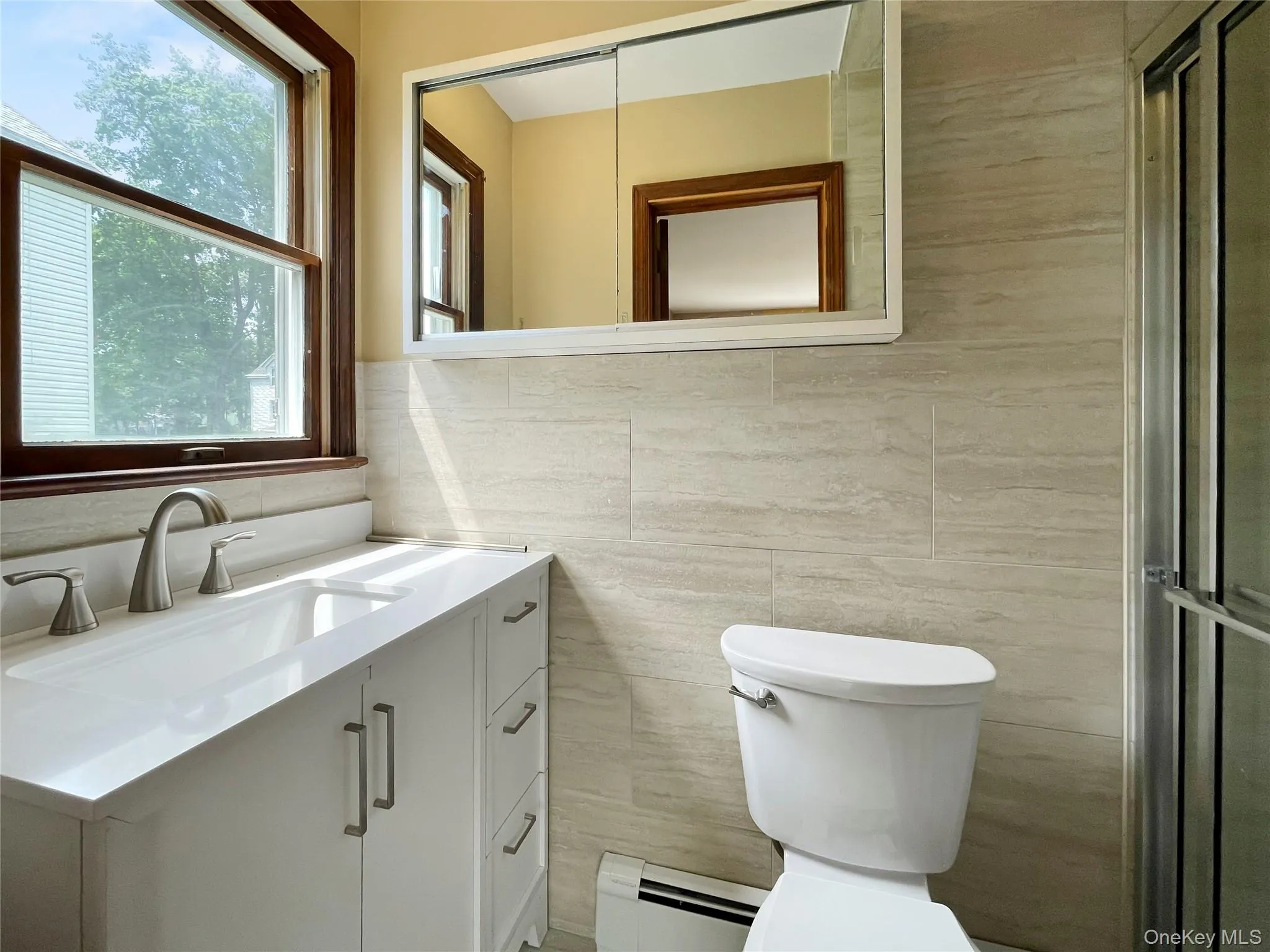Bathroom with tile walls, baseboard heating, plenty of natural light, vanity, and a shower with door Bathroom with tile walls, baseboard heating, plenty of natural light, vanity, and a shower with door