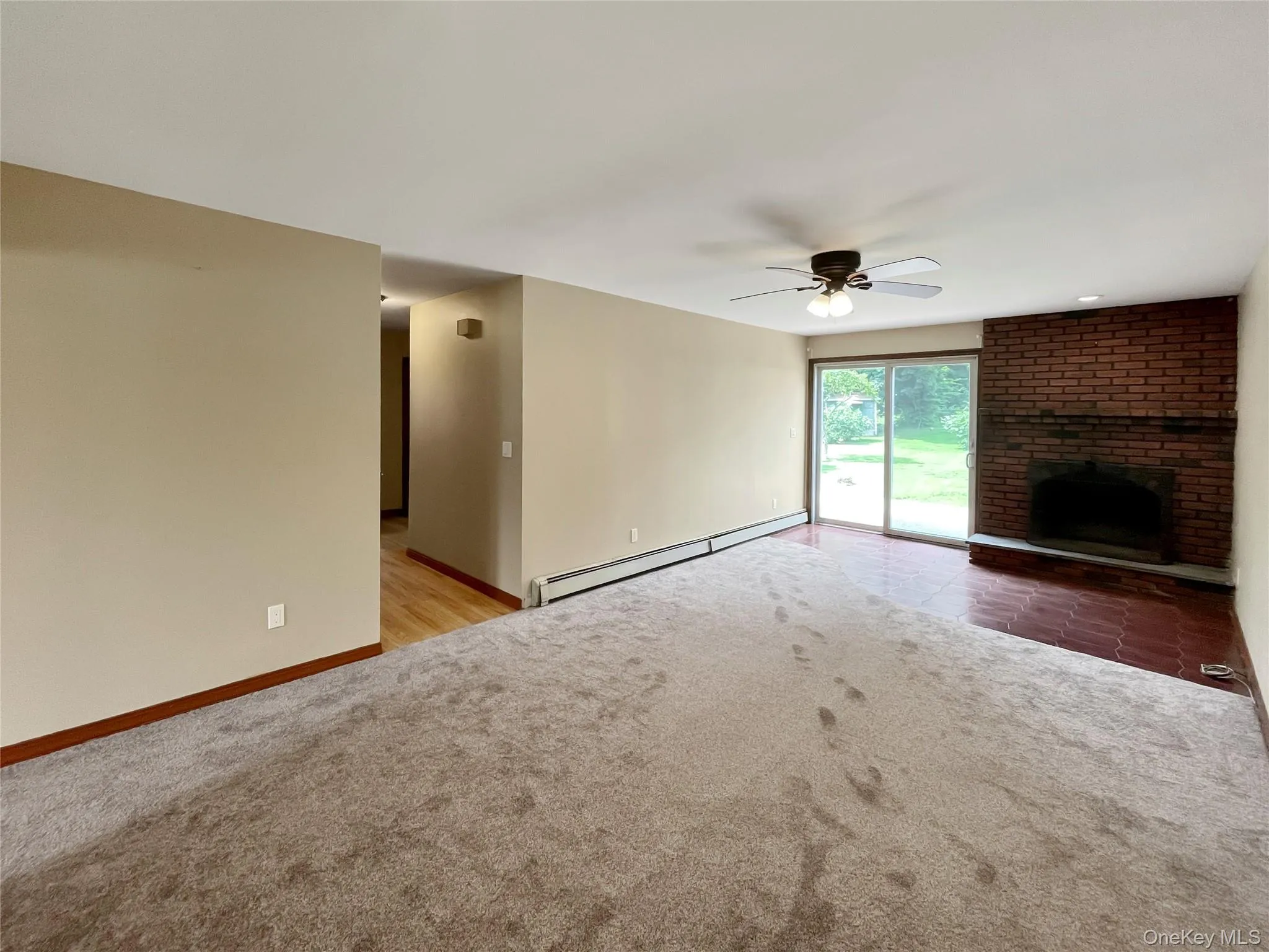 Unfurnished living room with carpet flooring, baseboard heating, a ceiling fan, and a fireplace Unfurnished living room with carpet flooring, baseboard heating, a ceiling fan, and a fireplace