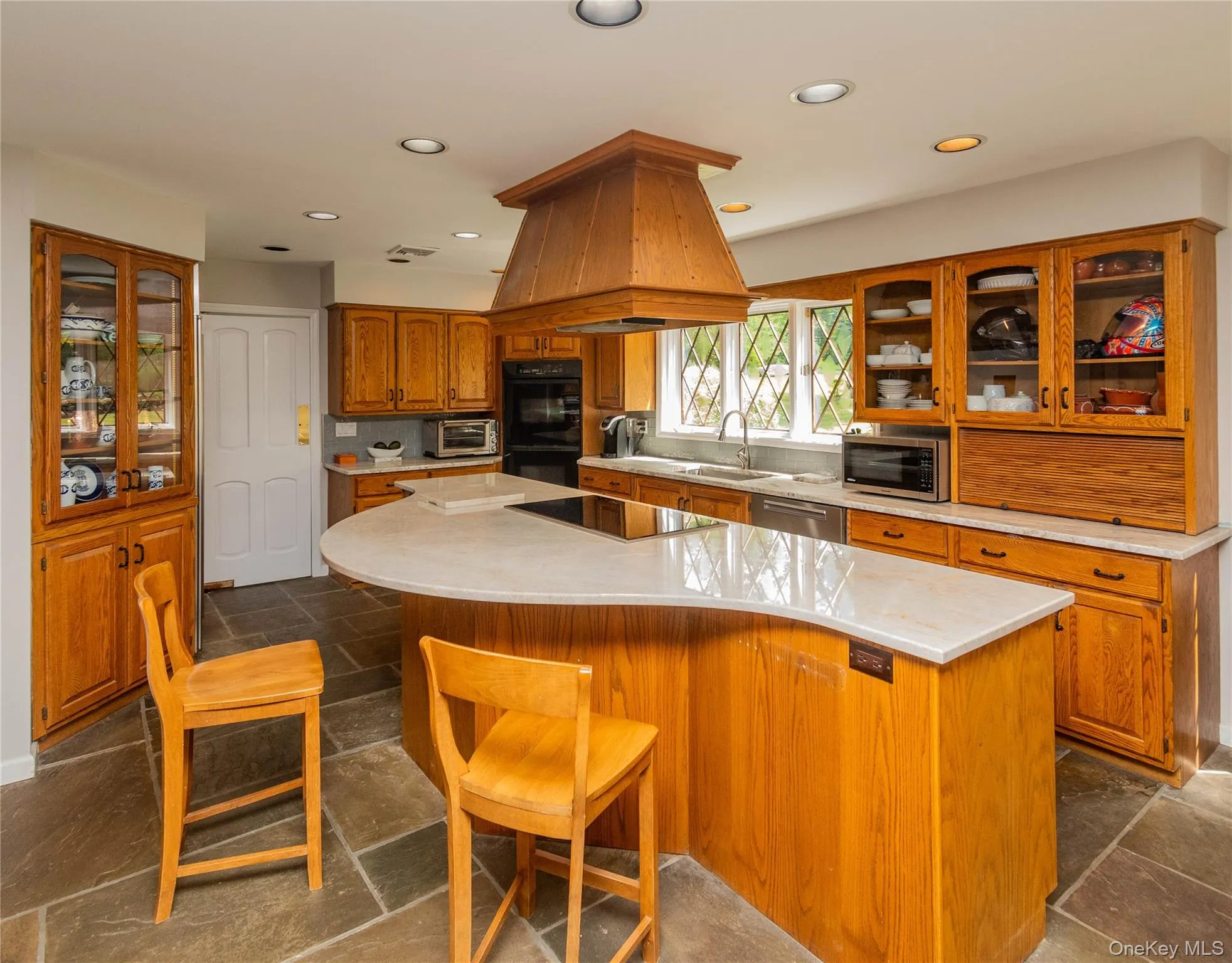 Kitchen with brown cabinets, recessed lighting, light countertops, glass insert cabinets, and a kitchen island Kitchen with brown cabinets, recessed lighting, light countertops, glass insert cabinets, and a kitchen island