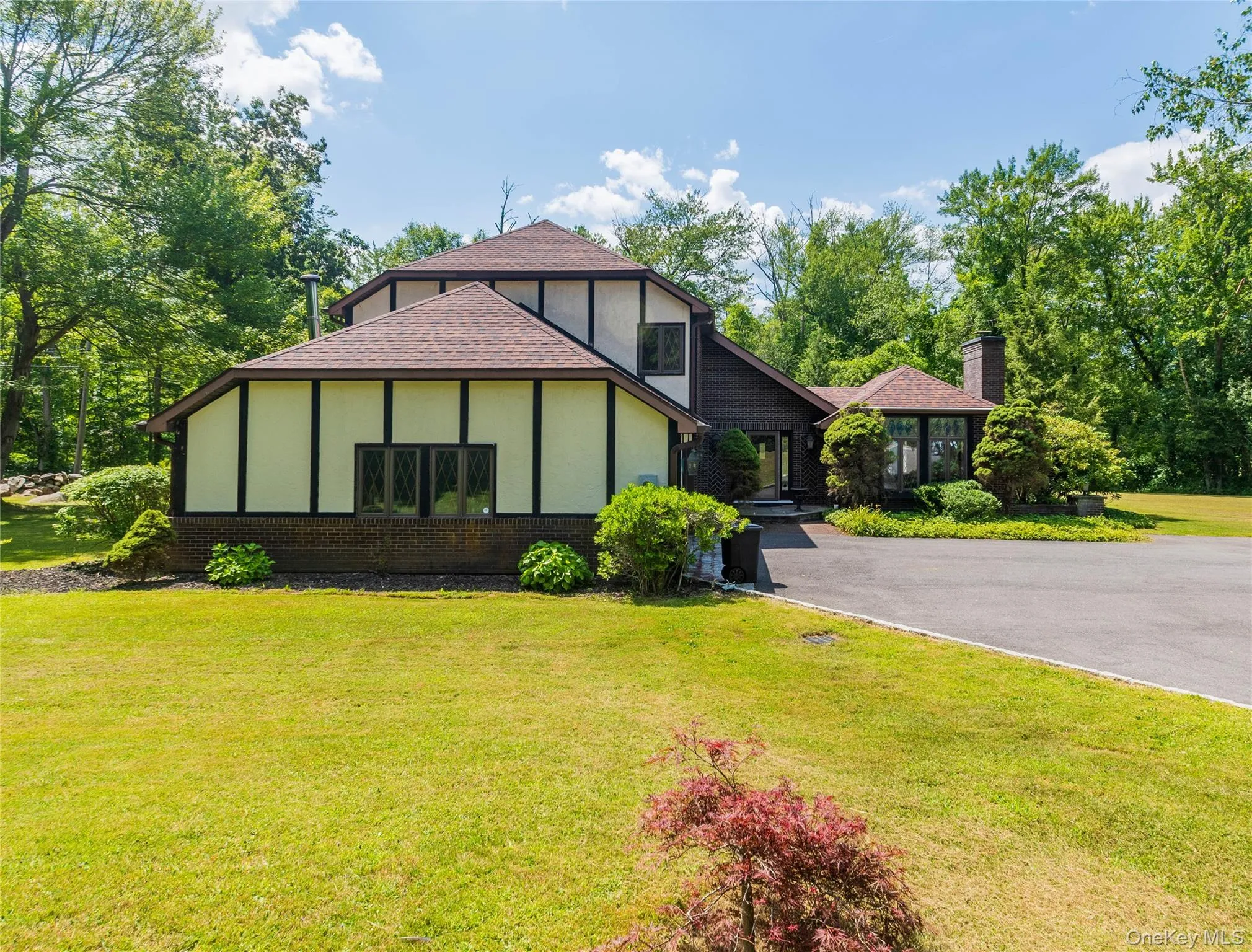 Tudor-style house featuring brick siding, stucco siding, a front lawn, a shingled roof, and driveway Tudor-style house featuring brick siding, stucco siding, a front lawn, a shingled roof, and driveway