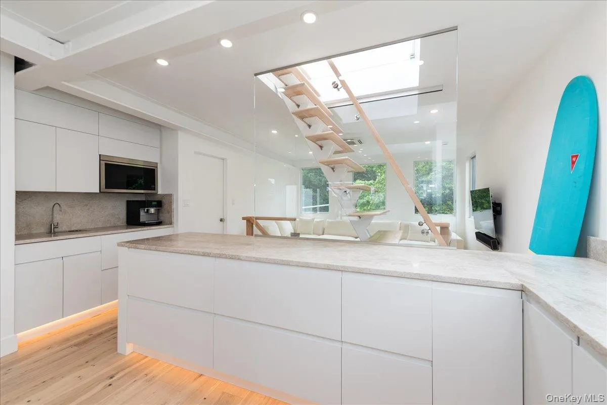 Kitchen featuring modern cabinets, decorative backsplash, light wood-style flooring, white cabinets, and stainless steel microwave Kitchen featuring modern cabinets, decorative backsplash, light wood-style flooring, white cabinets, and stainless steel microwave