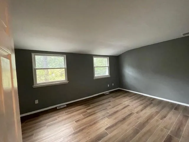 Empty room featuring wood finished floors and vaulted ceiling Empty room featuring wood finished floors and vaulted ceiling