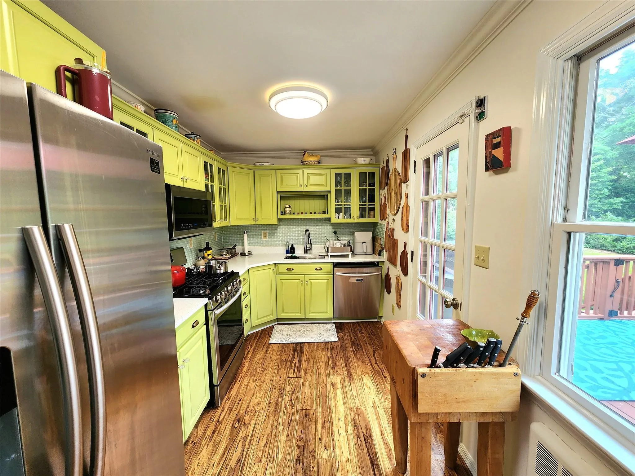 Kitchen with green cabinets, appliances with stainless steel finishes, dark wood finished floors, light countertops, and healthy amount of natural light Kitchen with green cabinets, appliances with stainless steel finishes, dark wood finished floors, light countertops, and healthy amount of natural light