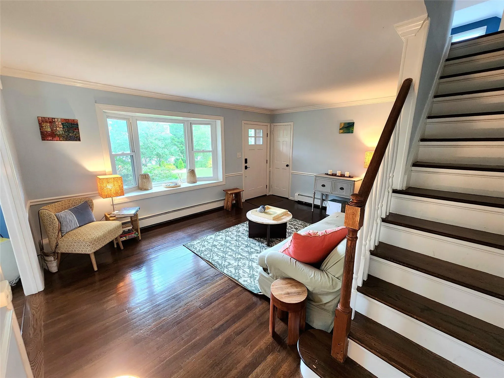 Living area featuring stairway, crown molding, wood finished floors, and baseboard heating Living area featuring stairway, crown molding, wood finished floors, and baseboard heating