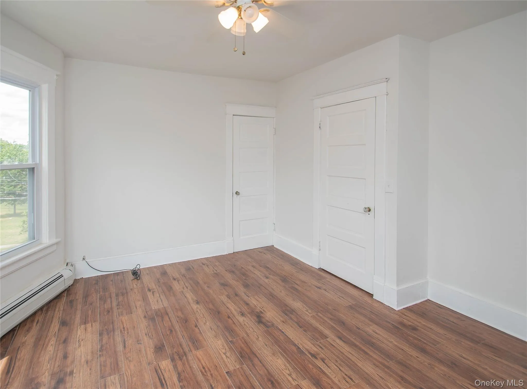 Spare room featuring wood finished floors, ceiling fan, and a baseboard radiator Spare room featuring wood finished floors, ceiling fan, and a baseboard radiator