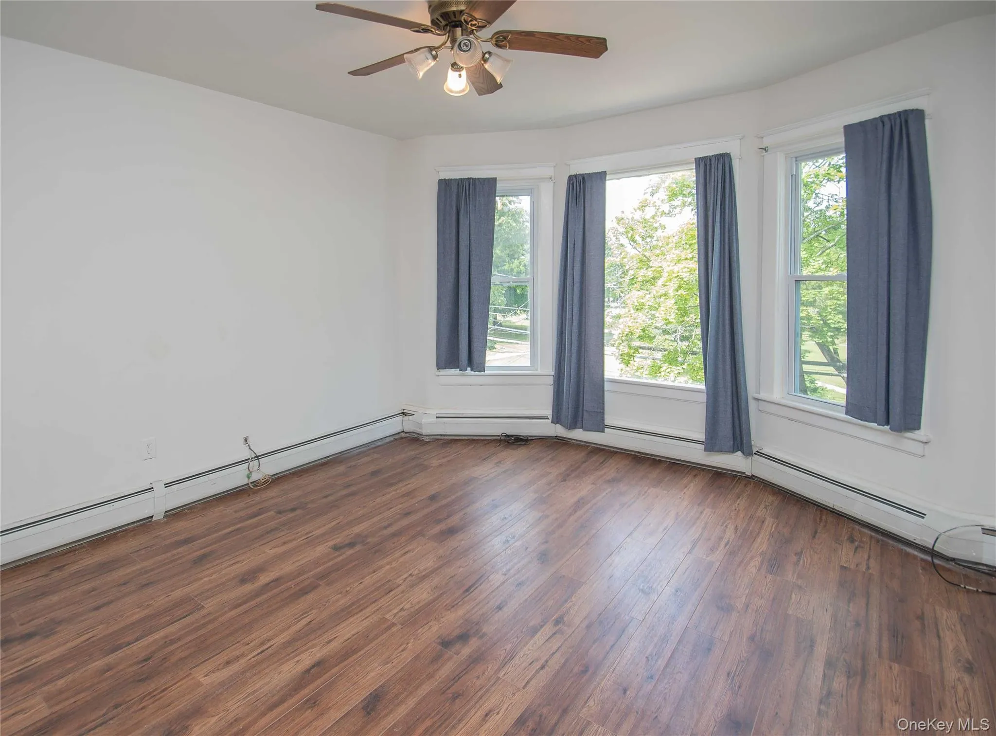 Unfurnished room with plenty of natural light, wood finished floors, a ceiling fan, and baseboard heating Unfurnished room with plenty of natural light, wood finished floors, a ceiling fan, and baseboard heating