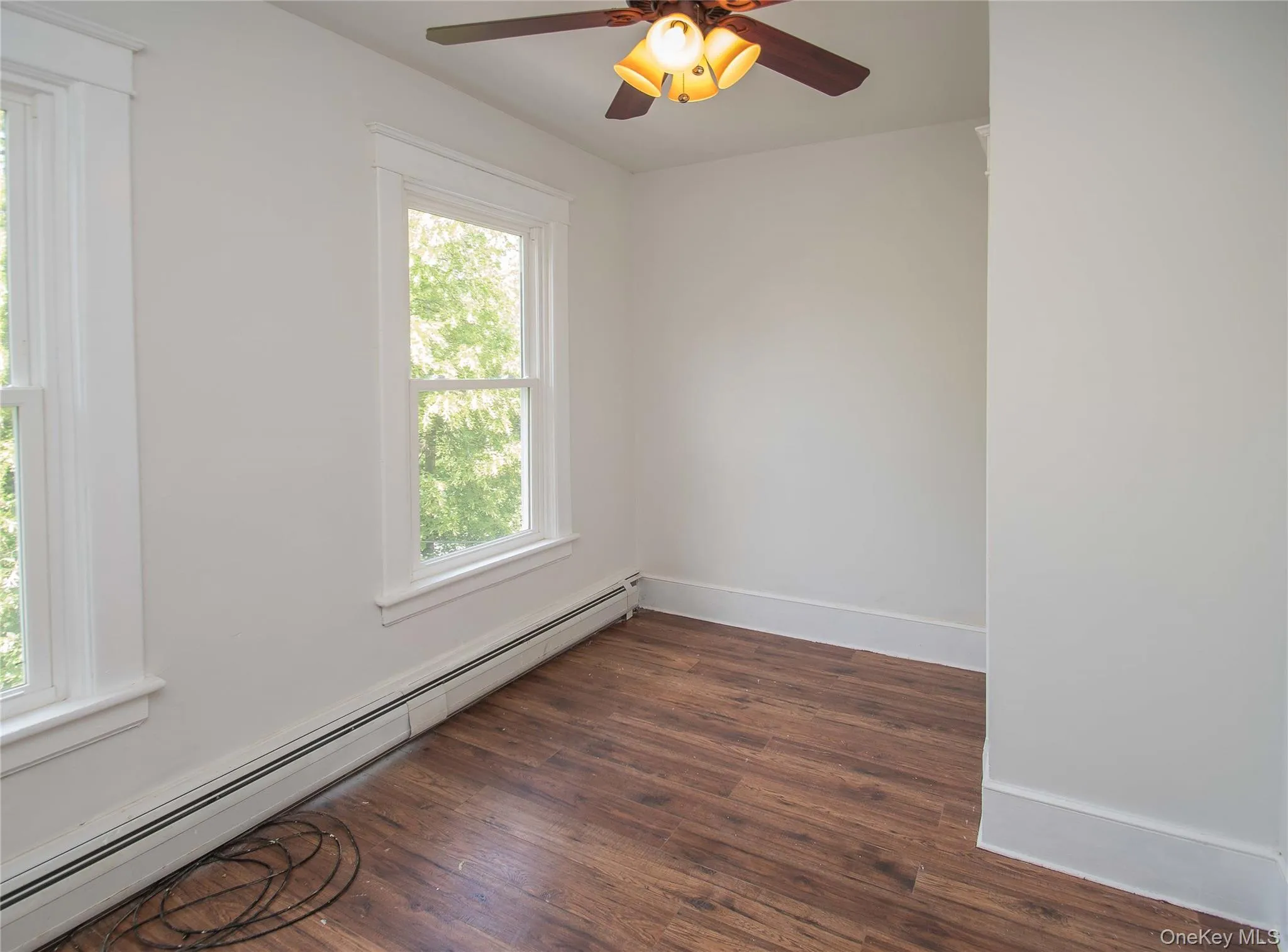 Spare room featuring a baseboard heating unit, dark wood finished floors, and ceiling fan Spare room featuring a baseboard heating unit, dark wood finished floors, and ceiling fan