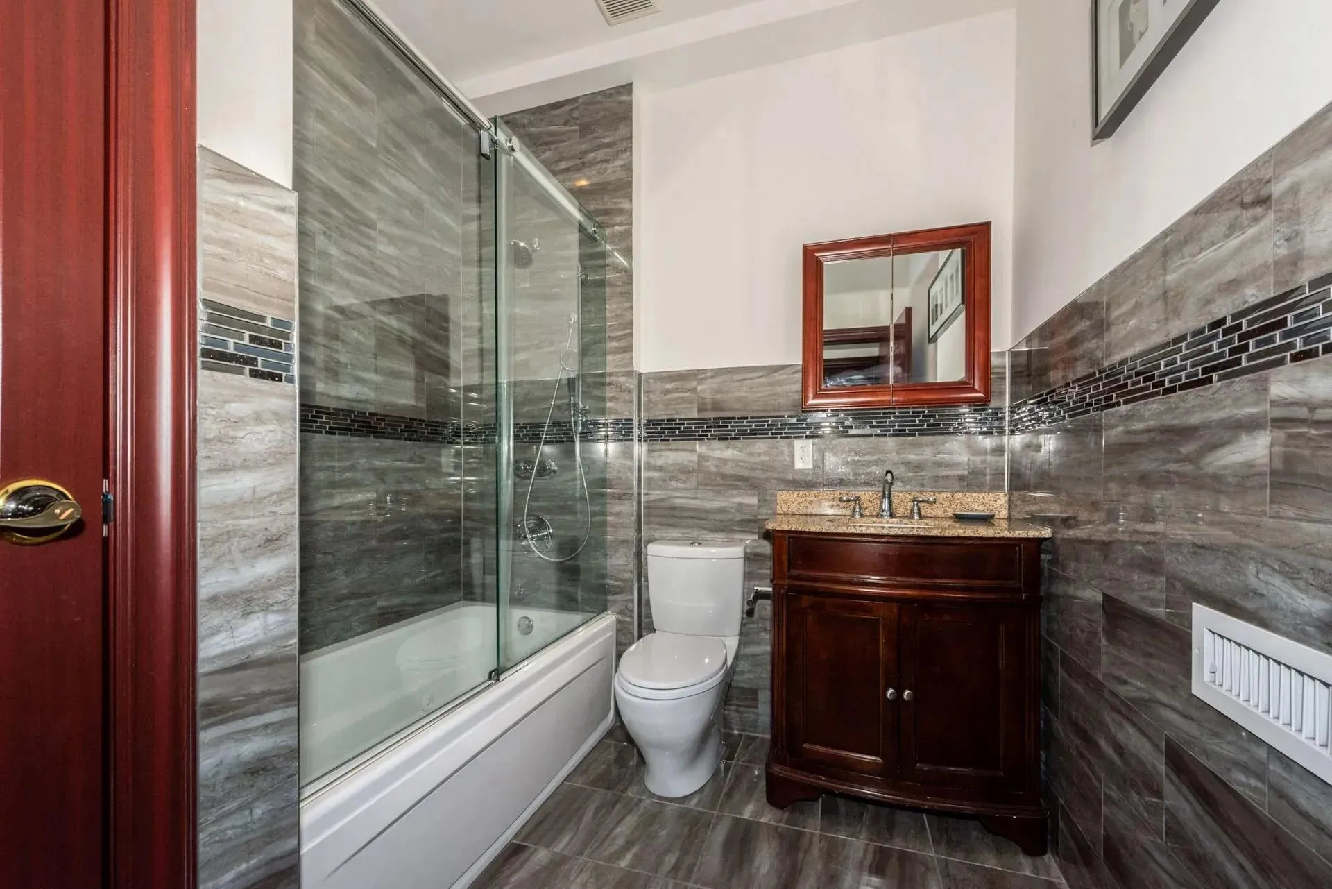 Bathroom featuring tile walls, bath / shower combo with glass door, vanity, and tile patterned flooring Bathroom featuring tile walls, bath / shower combo with glass door, vanity, and tile patterned flooring