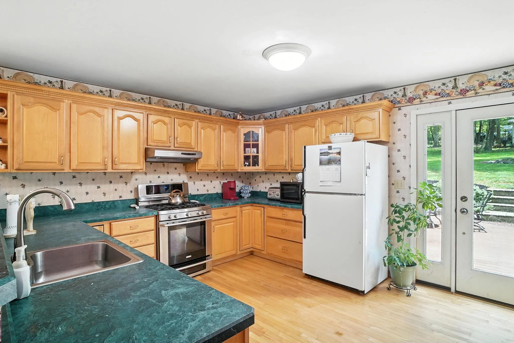 Kitchen featuring freestanding refrigerator, stainless steel gas range oven, dark countertops, glass insert cabinets, and light wood-style floors Kitchen featuring freestanding refrigerator, stainless steel gas range oven, dark countertops, glass insert cabinets, and light wood-style floors