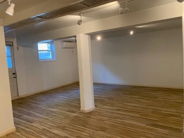 Basement featuring track lighting, wood finished floors, and a wall mounted AC Basement featuring track lighting, wood finished floors, and a wall mounted AC