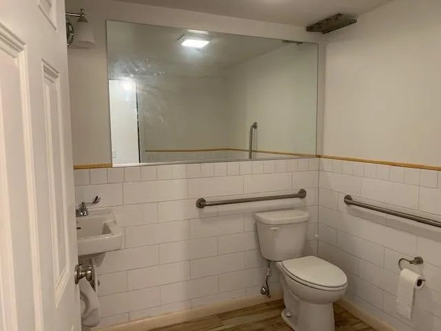 Bathroom featuring tile walls, a wainscoted wall, and wood finished floors Bathroom featuring tile walls, a wainscoted wall, and wood finished floors