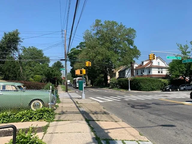 View of asphalt road featuring traffic lights, sidewalks, curbs, street lighting, and traffic signs View of asphalt road featuring traffic lights, sidewalks, curbs, street lighting, and traffic signs