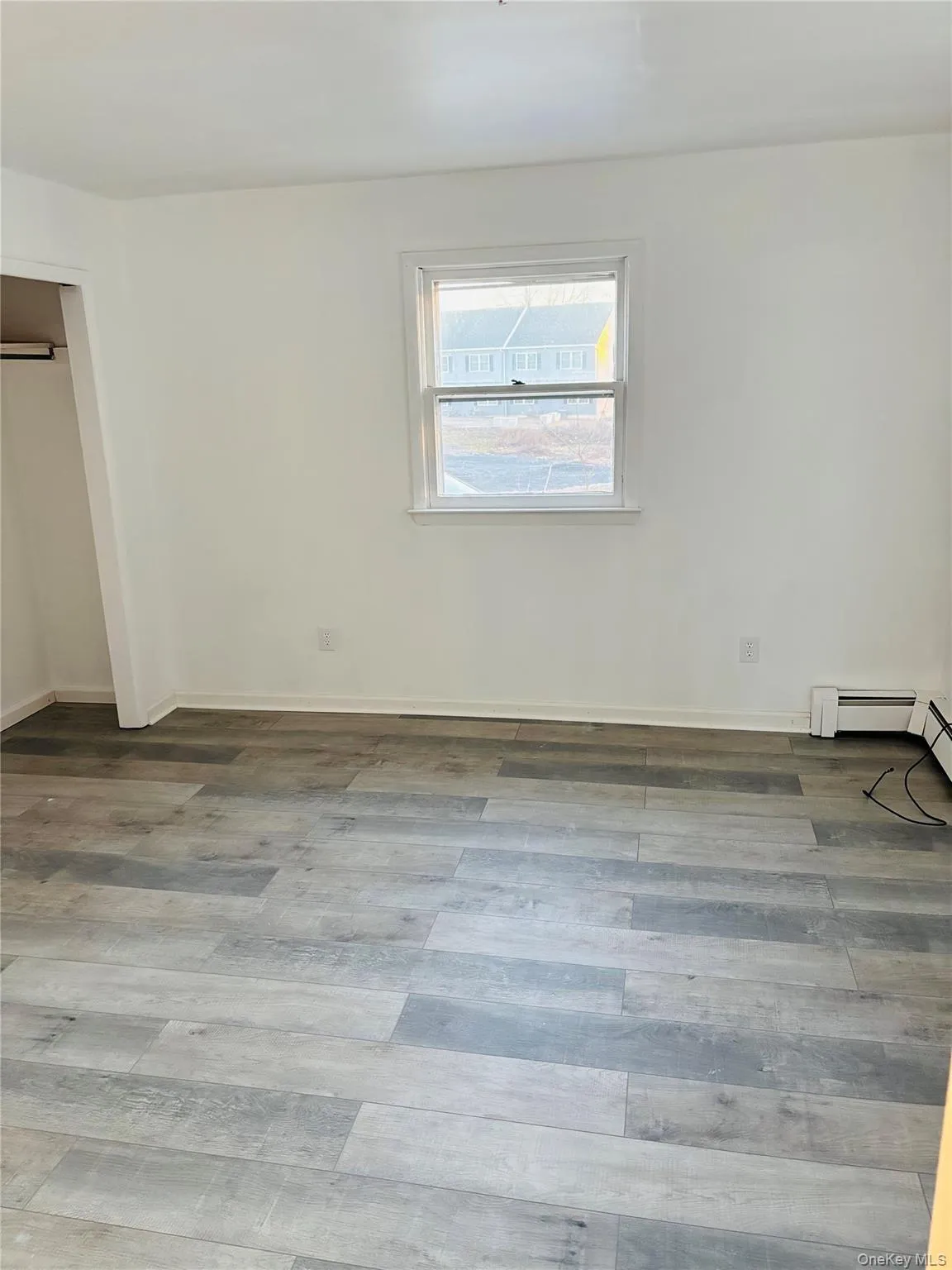 Unfurnished bedroom featuring a closet, wood finished floors, and baseboard heating Unfurnished bedroom featuring a closet, wood finished floors, and baseboard heating