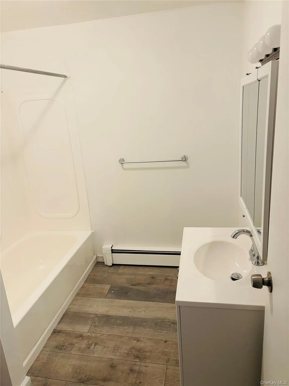 Full bathroom with vanity, a baseboard heating unit, dark wood-style flooring, and shower / tub combination Full bathroom with vanity, a baseboard heating unit, dark wood-style flooring, and shower / tub combination