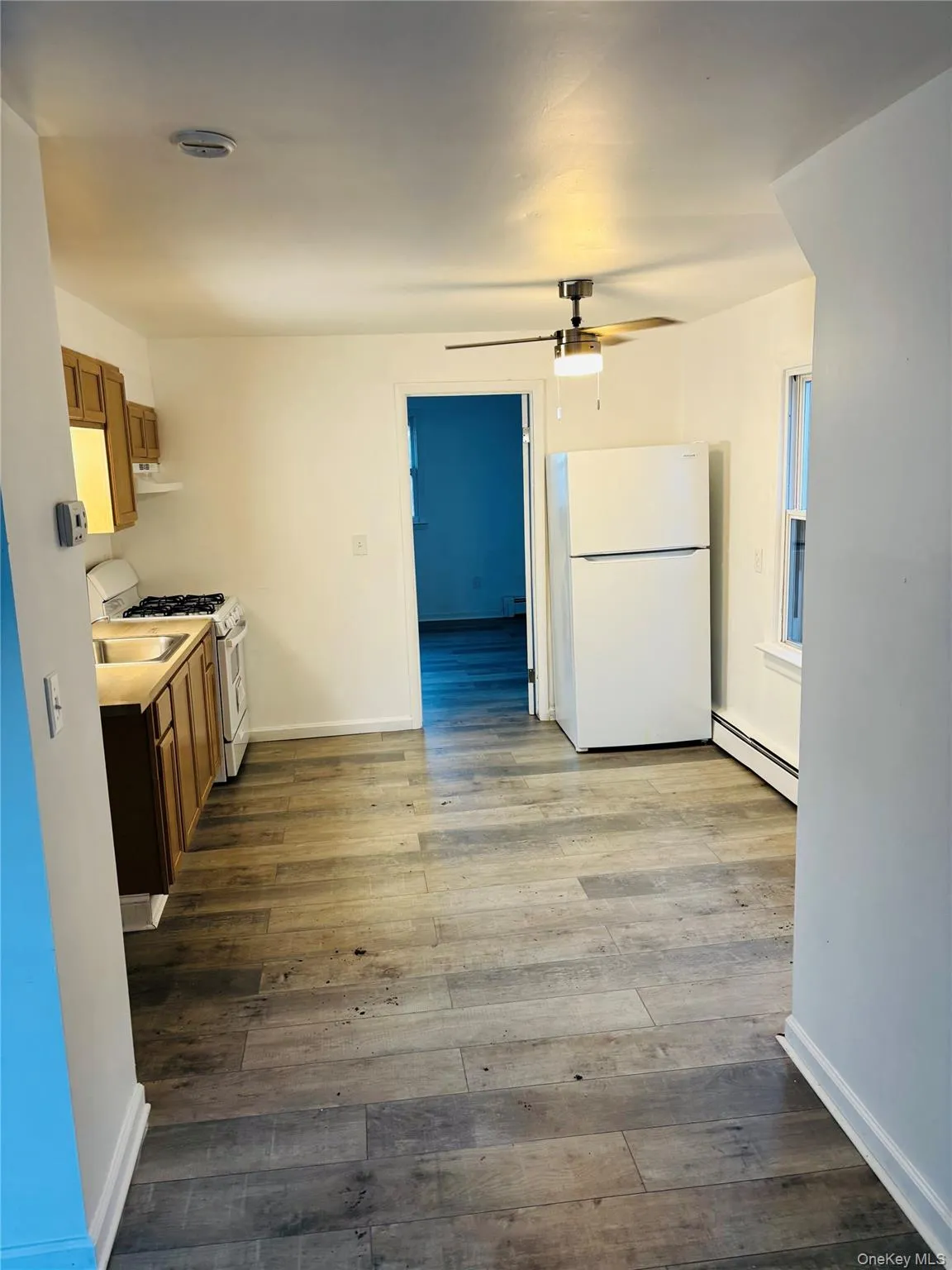 Kitchen featuring white appliances, brown cabinetry, light countertops, baseboard heating, and dark wood-style floors Kitchen featuring white appliances, brown cabinetry, light countertops, baseboard heating, and dark wood-style floors