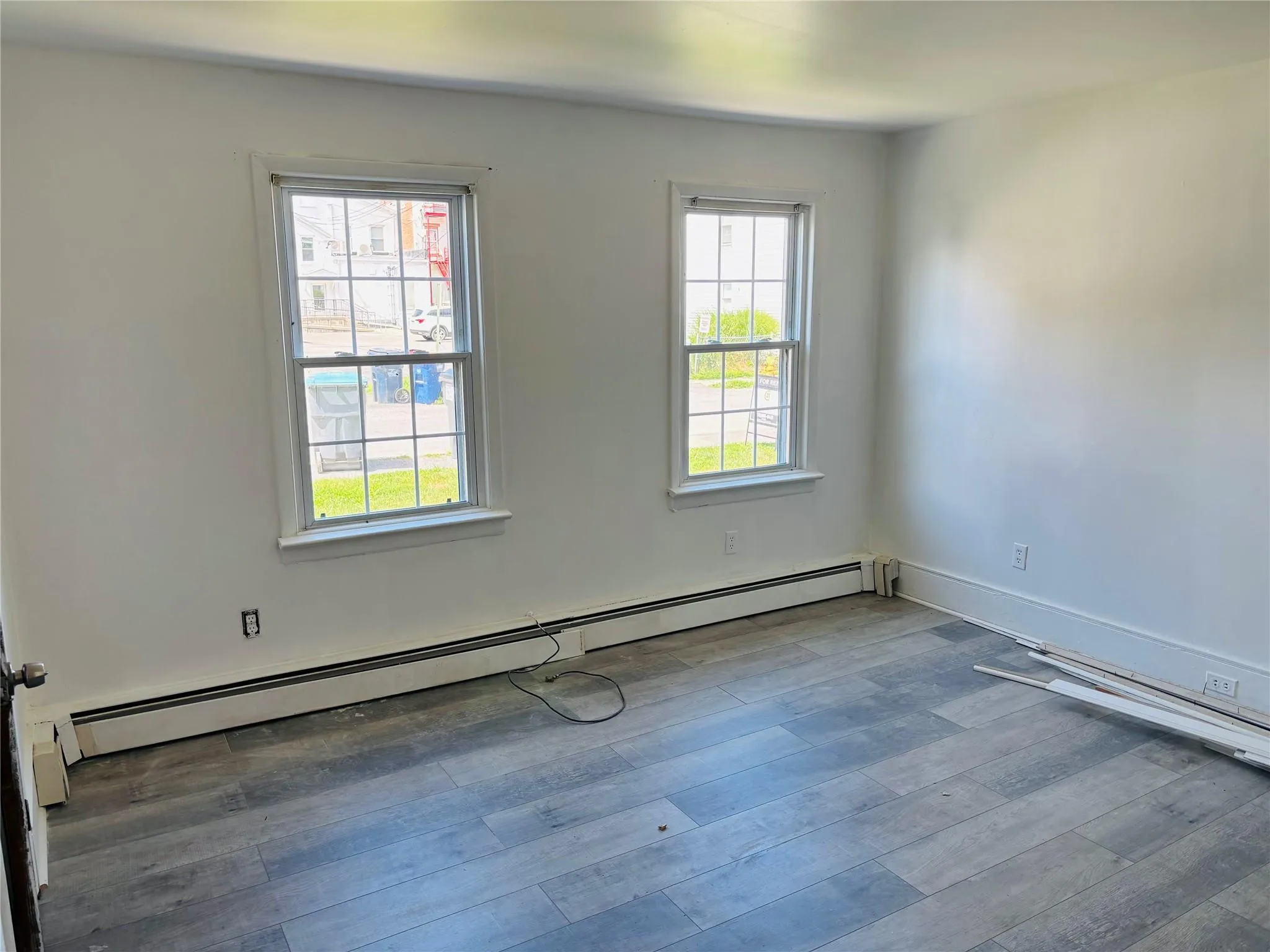 Unfurnished room with baseboard heating, plenty of natural light, and wood finished floors Unfurnished room with baseboard heating, plenty of natural light, and wood finished floors