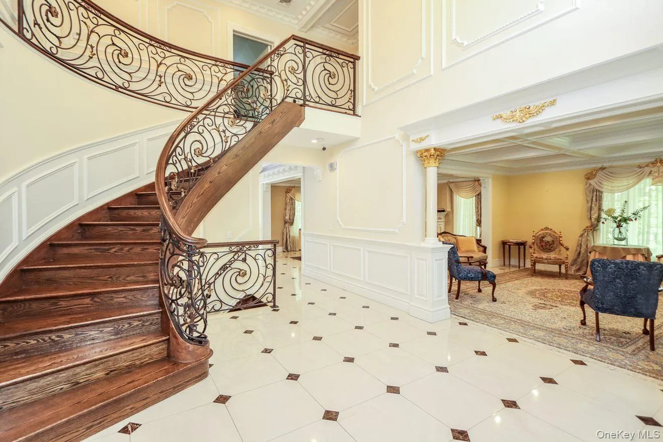 Staircase featuring a decorative wall, tile patterned flooring, beamed ceiling, ornamental molding, and a high ceiling Staircase featuring a decorative wall, tile patterned flooring, beamed ceiling, ornamental molding, and a high ceiling