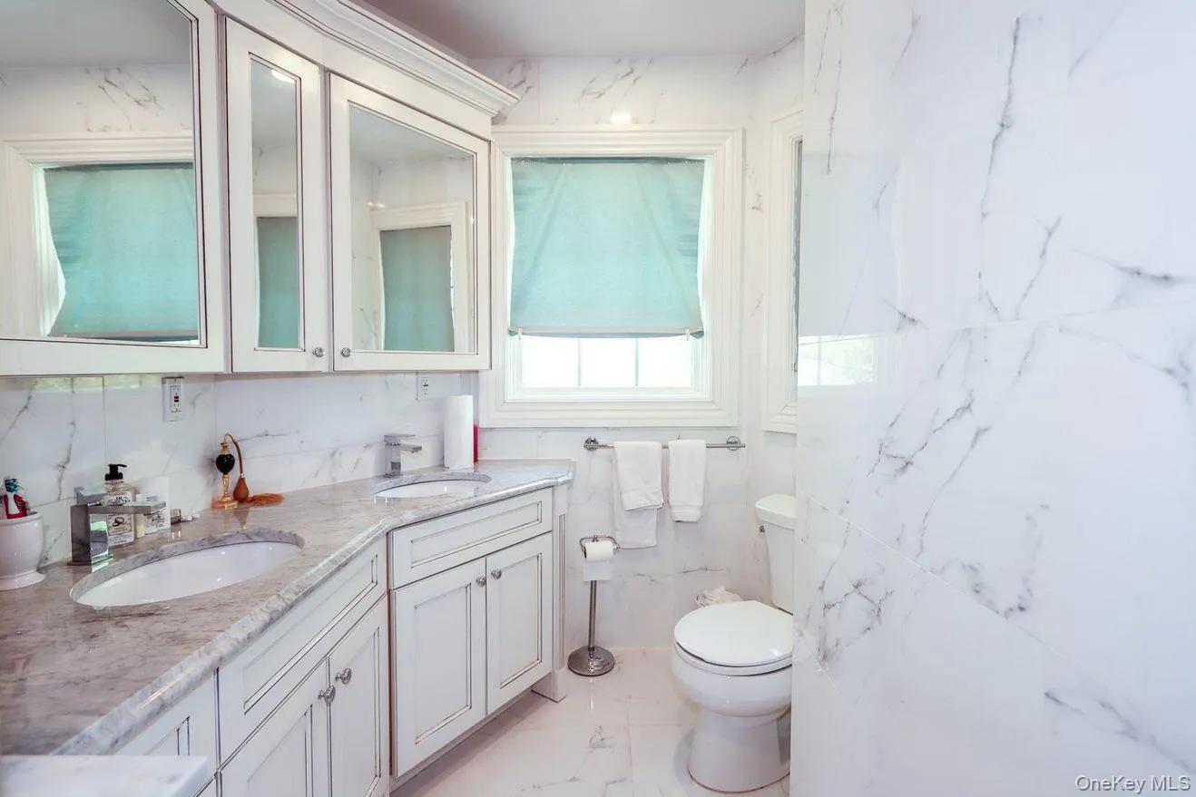 Full bath featuring marble look tiles and double vanity Full bath featuring marble look tiles and double vanity