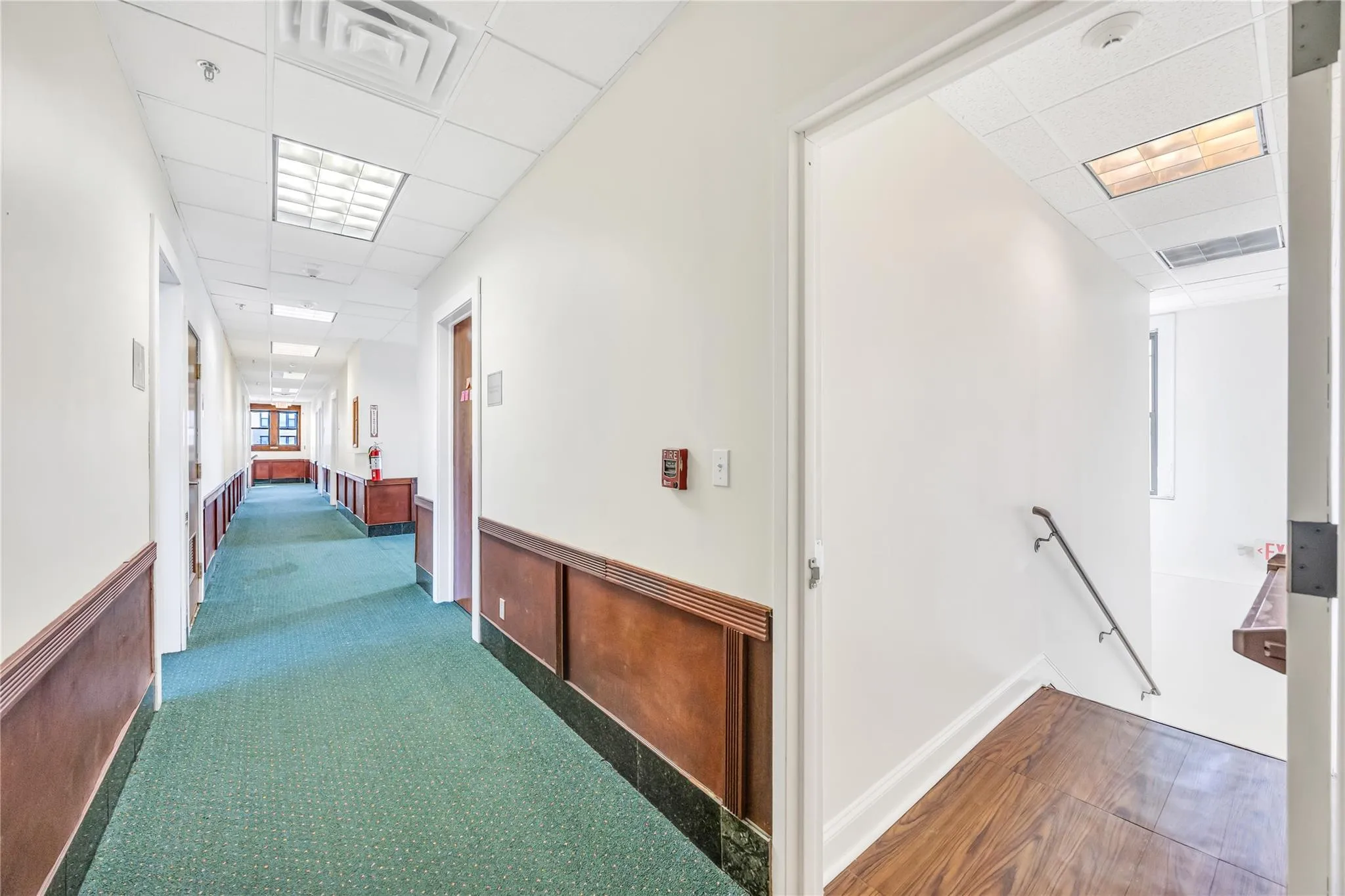 Hallway featuring a drop ceiling, an upstairs landing, and carpet flooring Hallway featuring a drop ceiling, an upstairs landing, and carpet flooring