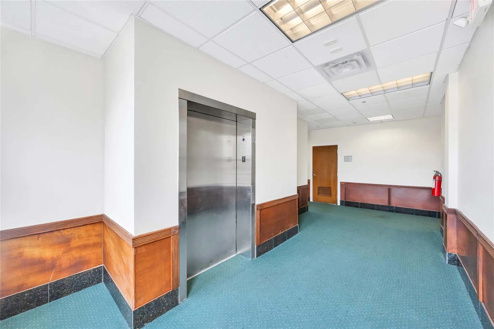 Spare room featuring a wainscoted wall, elevator, a drop ceiling, and carpet flooring Spare room featuring a wainscoted wall, elevator, a drop ceiling, and carpet flooring
