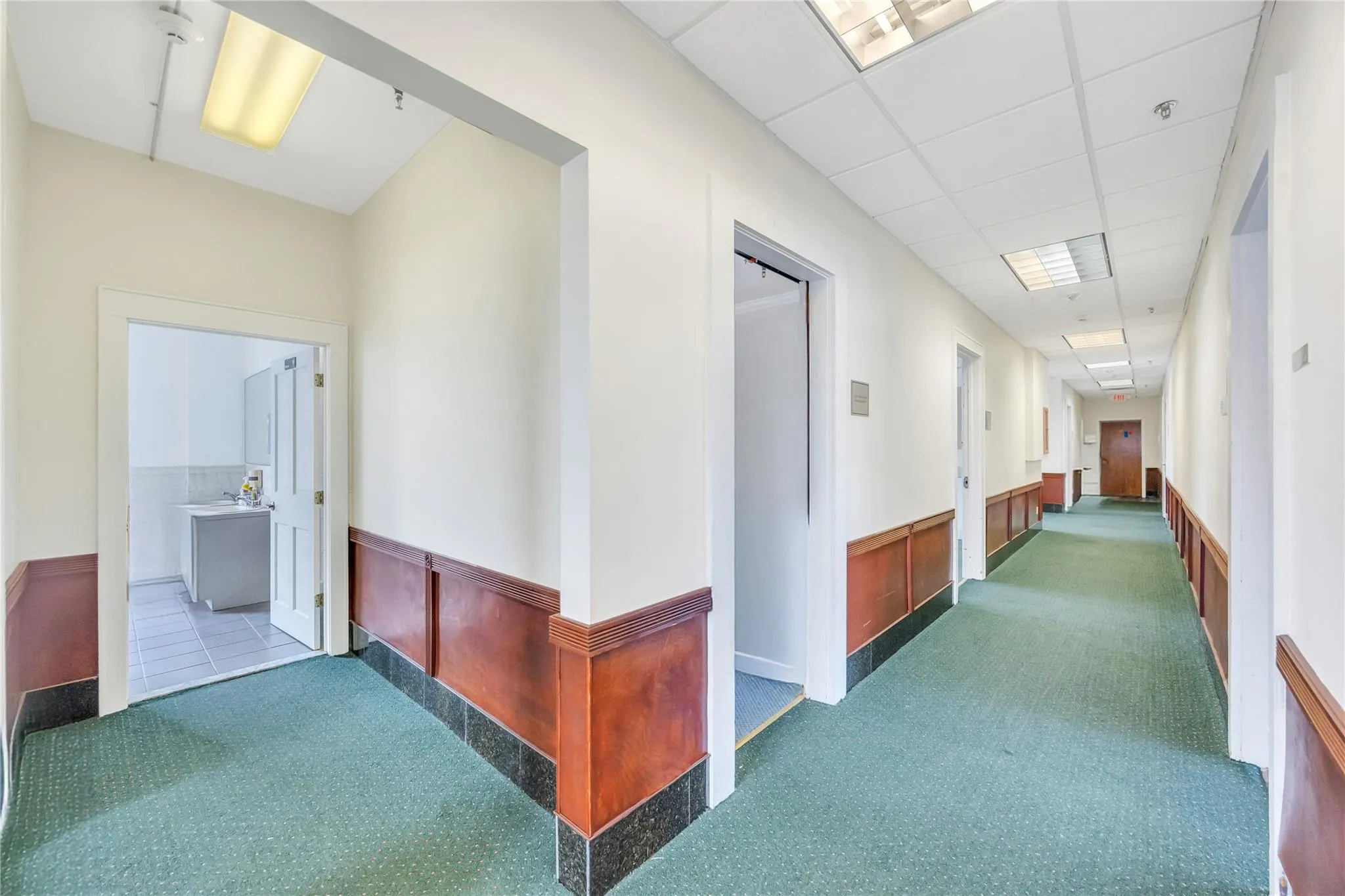 Corridor featuring carpet floors, a wainscoted wall, and a drop ceiling Corridor featuring carpet floors, a wainscoted wall, and a drop ceiling