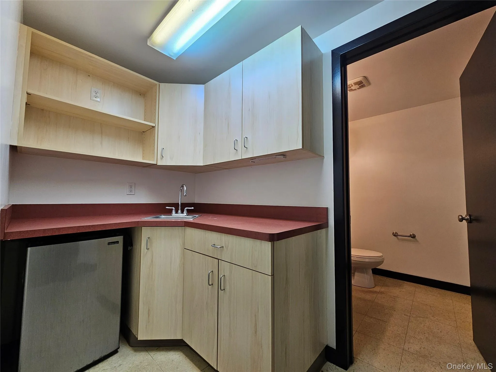 Kitchen featuring dark countertops, open shelves, stainless steel fridge, and light brown cabinets Kitchen featuring dark countertops, open shelves, stainless steel fridge, and light brown cabinets