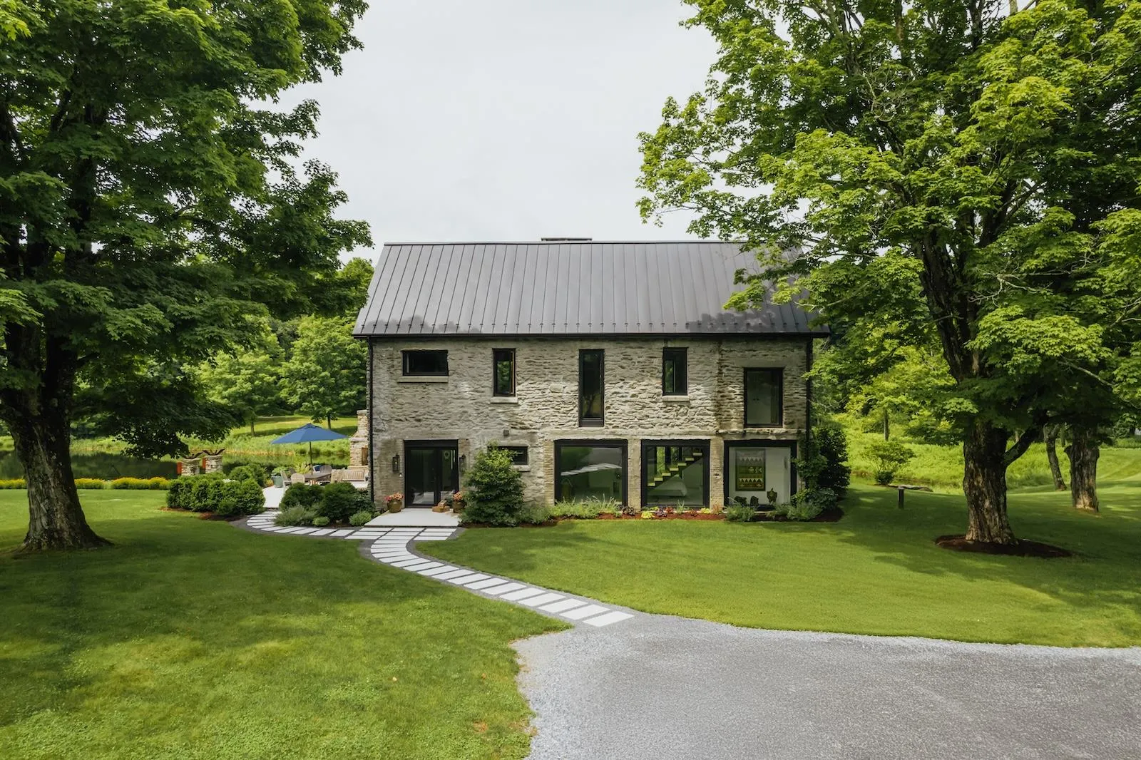 View of front of home featuring stone siding, a front yard, and a metal roof View of front of home featuring stone siding, a front yard, and a metal roof