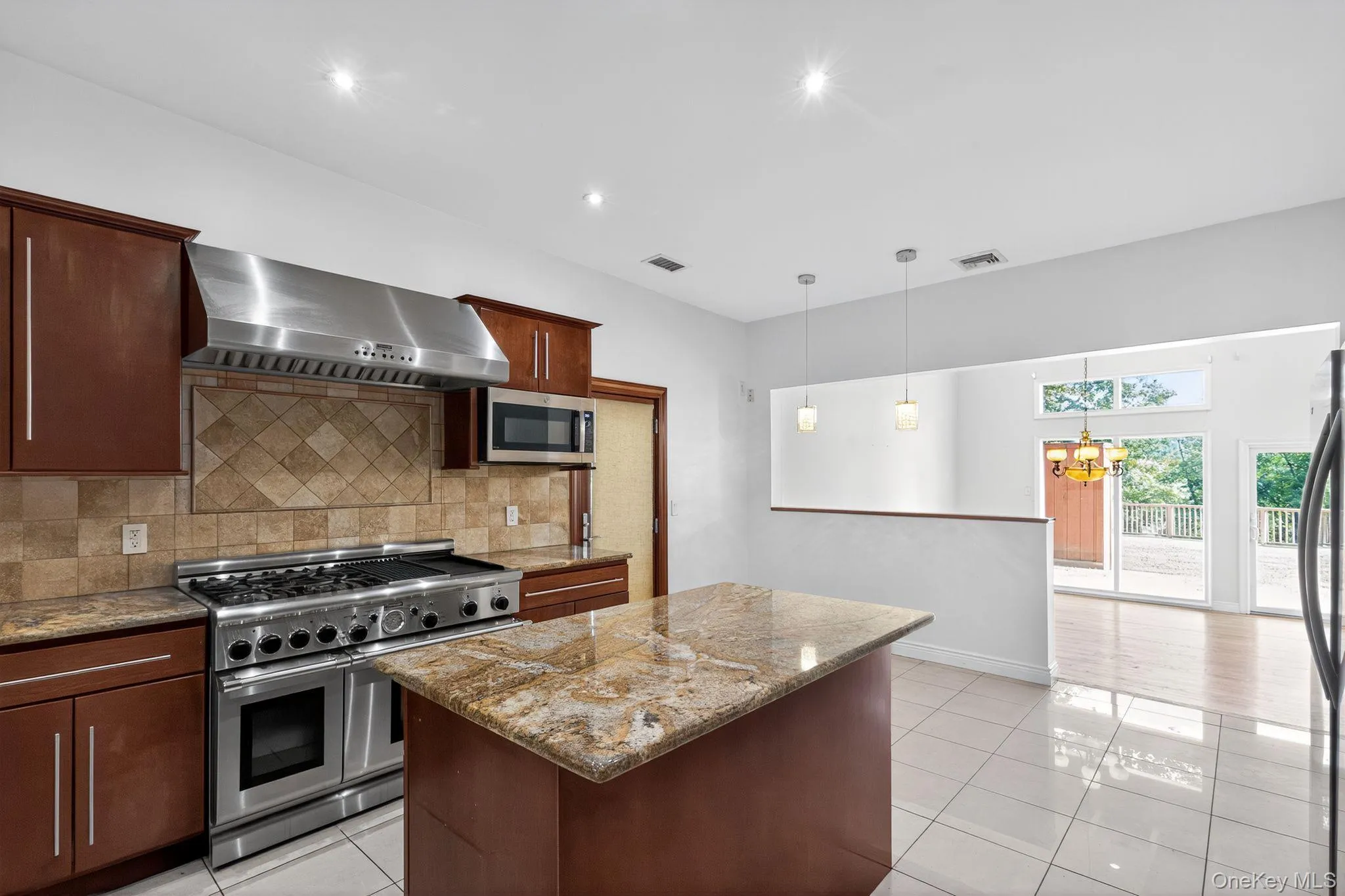 Kitchen featuring appliances with stainless steel finishes, wall chimney exhaust hood, tasteful backsplash, light tile patterned floors, and a center island Kitchen featuring appliances with stainless steel finishes, wall chimney exhaust hood, tasteful backsplash, light tile patterned floors, and a center island