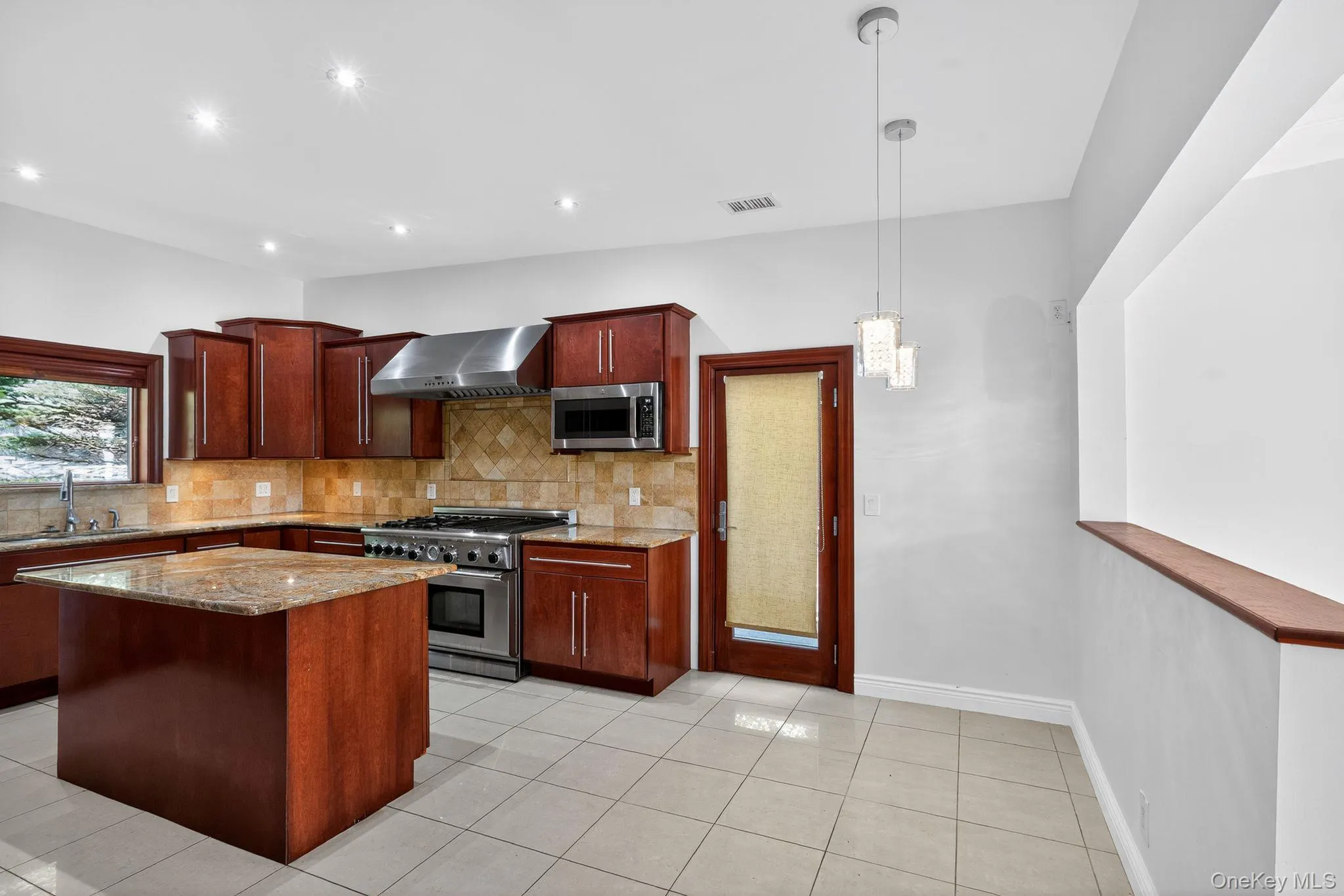 Kitchen with decorative light fixtures, light stone counters, appliances with stainless steel finishes, wall chimney range hood, and decorative backsplash Kitchen with decorative light fixtures, light stone counters, appliances with stainless steel finishes, wall chimney range hood, and decorative backsplash