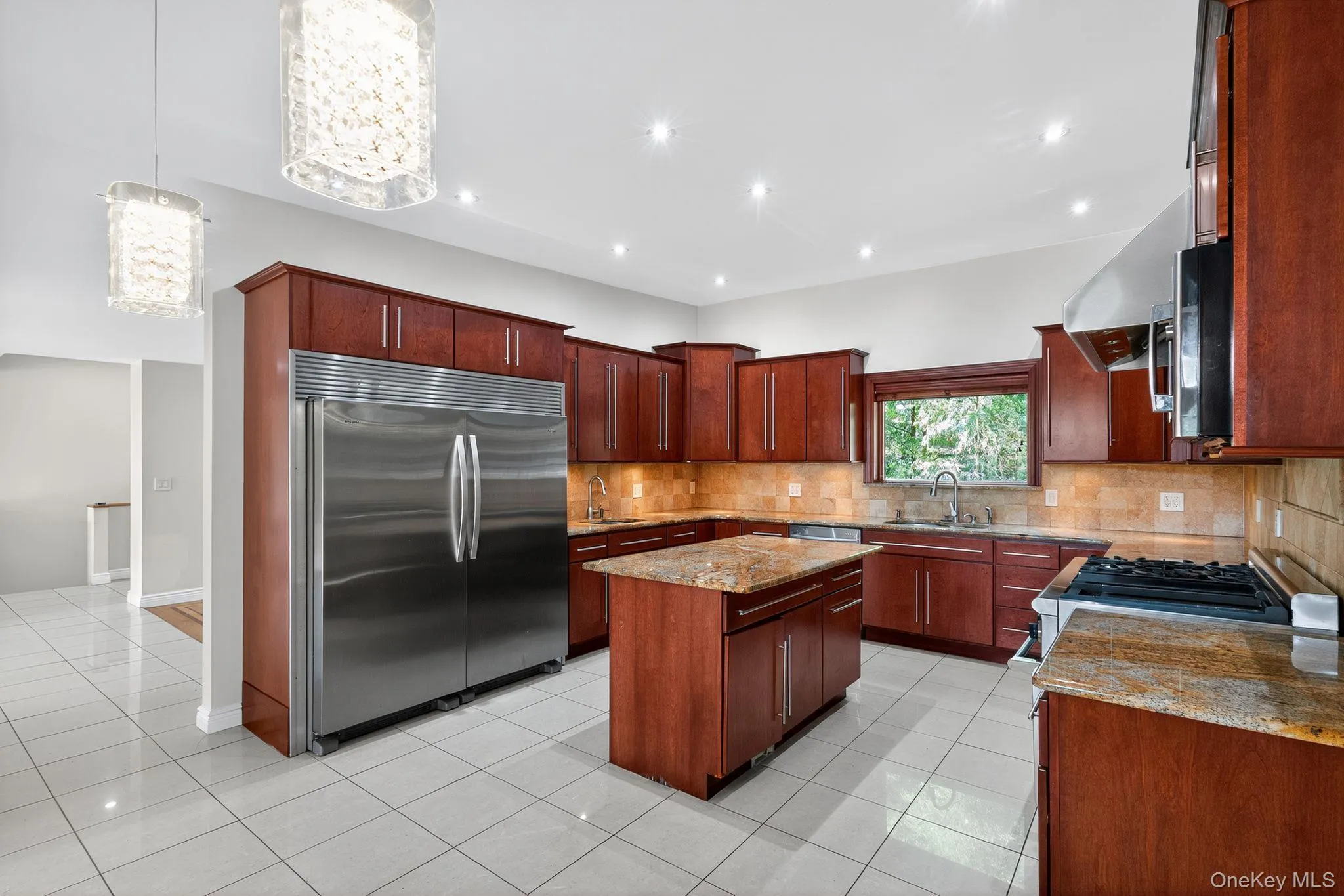 Kitchen with a center island, stainless steel appliances, light stone counters, decorative light fixtures, and tasteful backsplash Kitchen with a center island, stainless steel appliances, light stone counters, decorative light fixtures, and tasteful backsplash